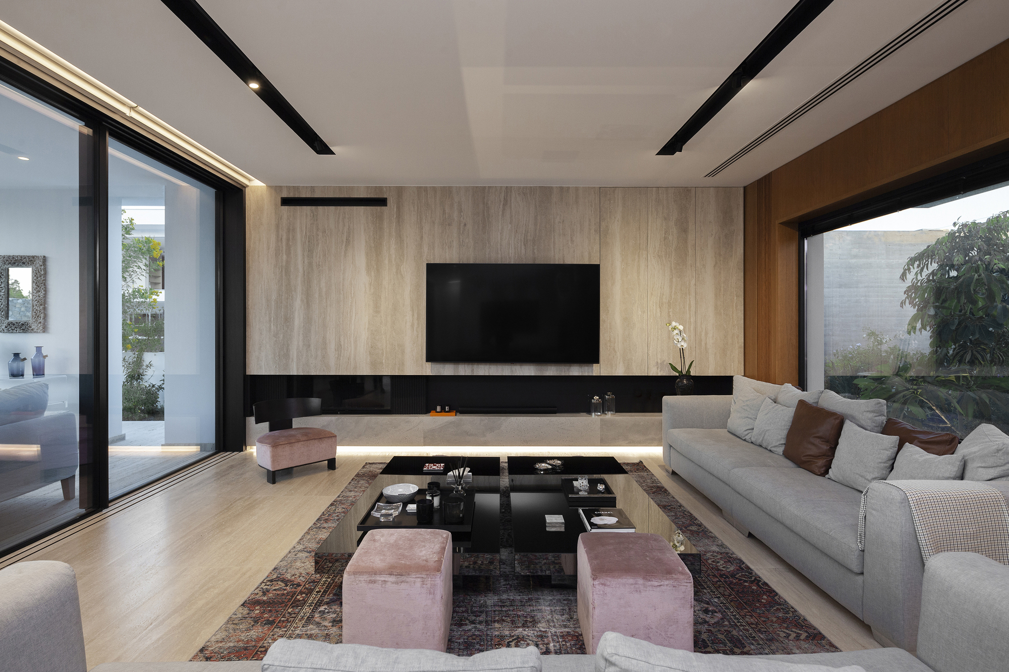 Living space with floating media console beneath wood-clad wall and corner glazing framing garden views at dusk