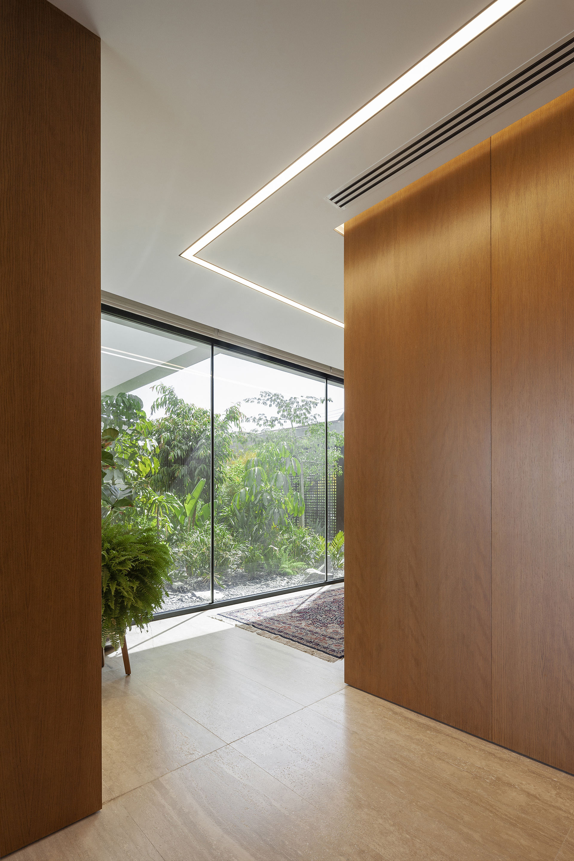 Wood-paneled corridor with angled ceiling light fixture and glazed opening onto garden courtyard