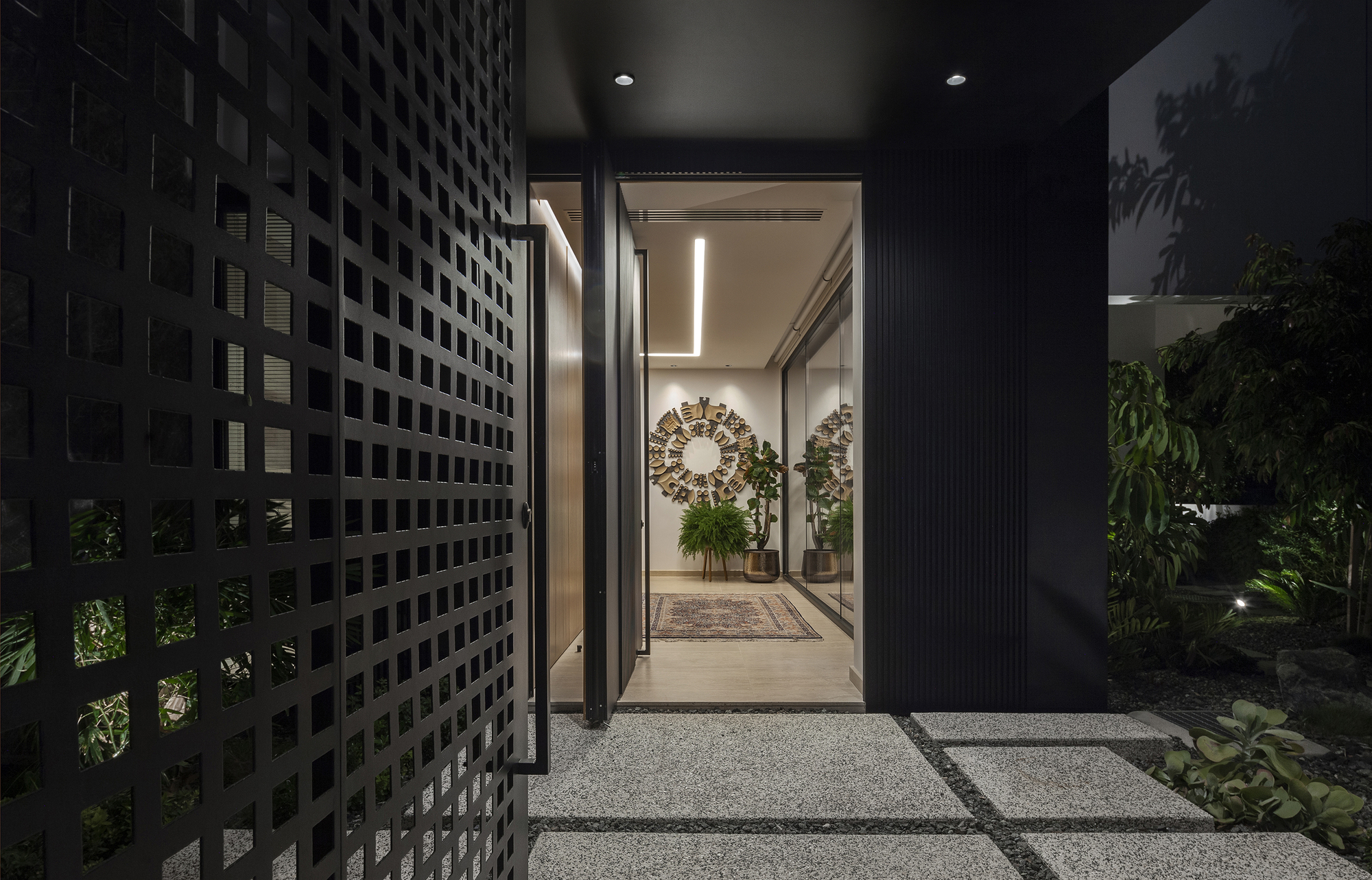 Entry path with perforated screen wall and planted garden beds illuminated at night