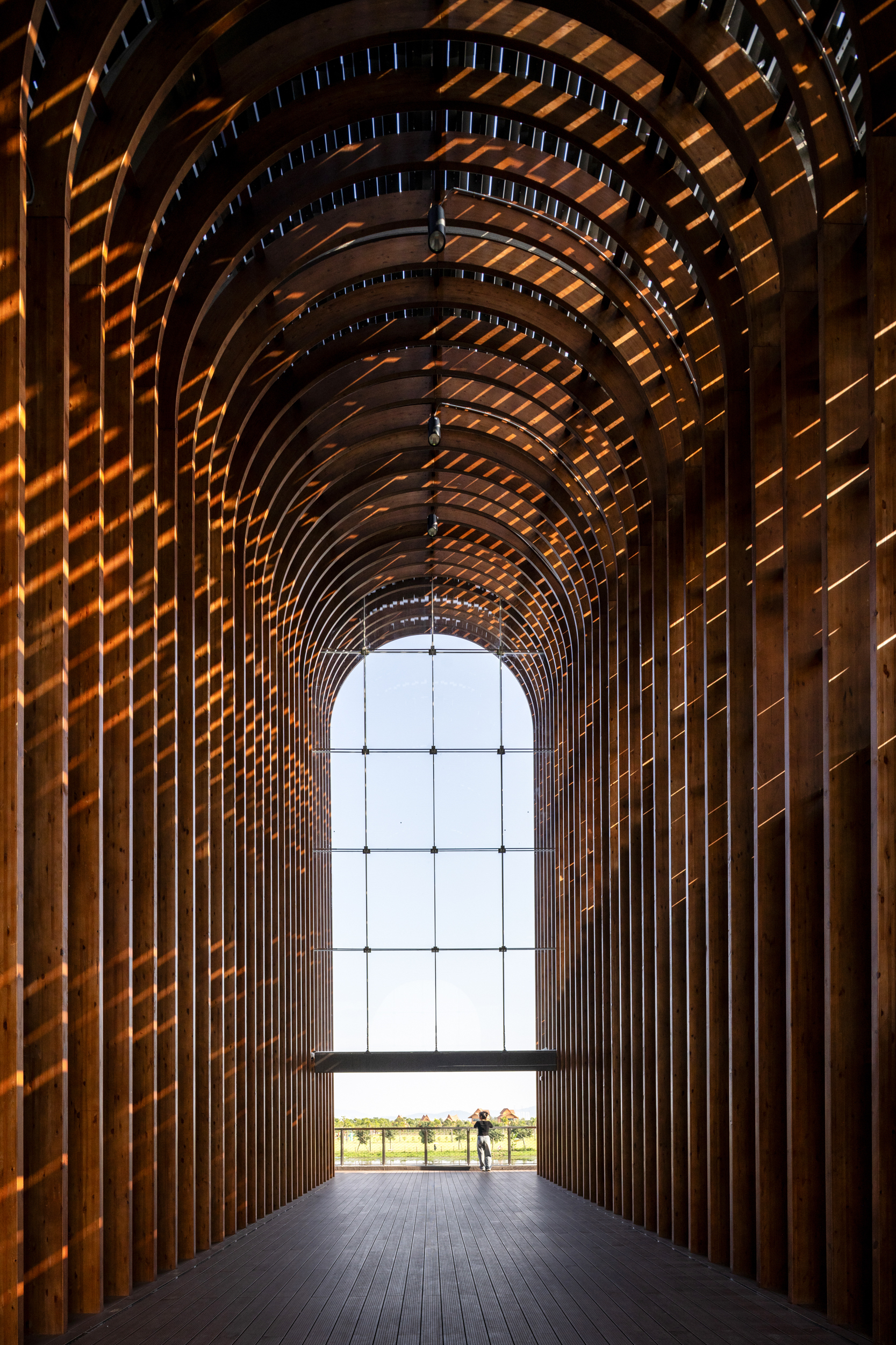 Interior view through vaulted timber rib arcade toward glazed opening with silhouetted figure
