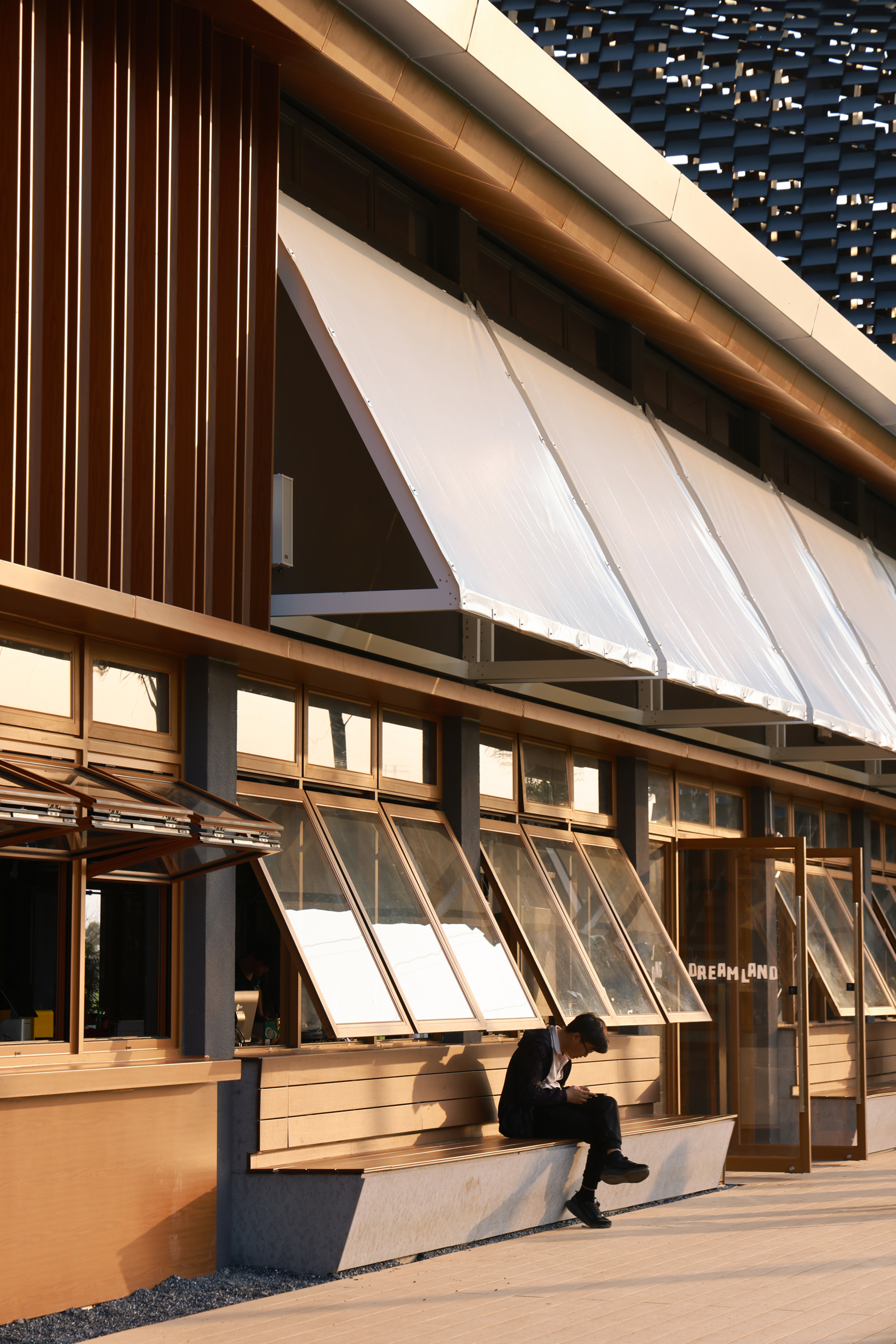 Hinged glazed panels below timber soffits where a person sits on a concrete bench