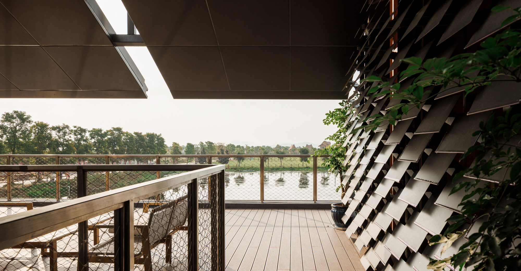 Timber deck terrace overlooking a pond with vine-covered angled metal screen beyond