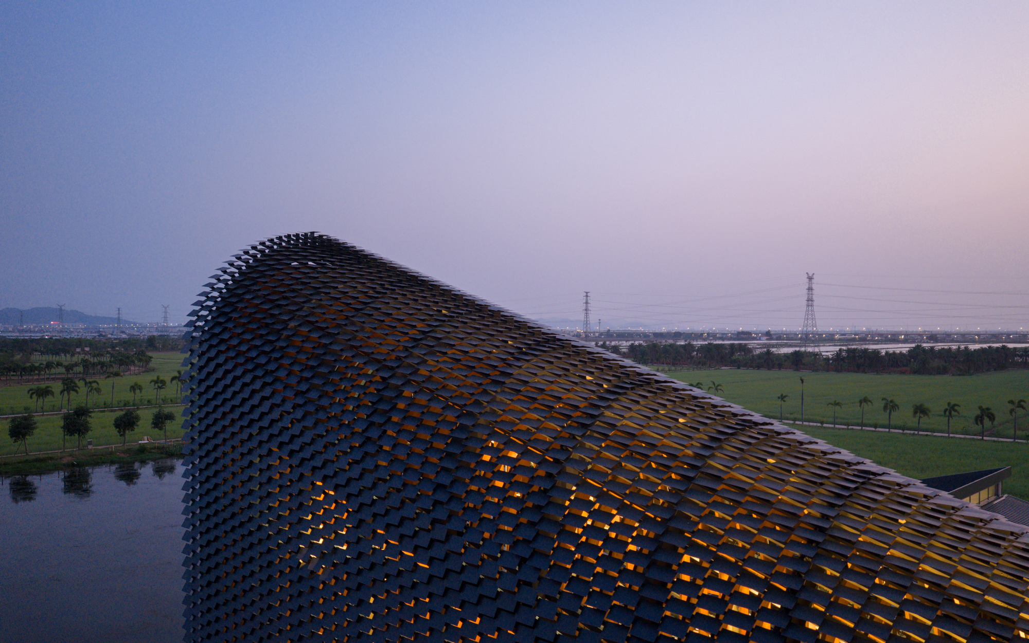 Drone view of the perforated tile roof structure illuminated from within at dusk over rice paddies