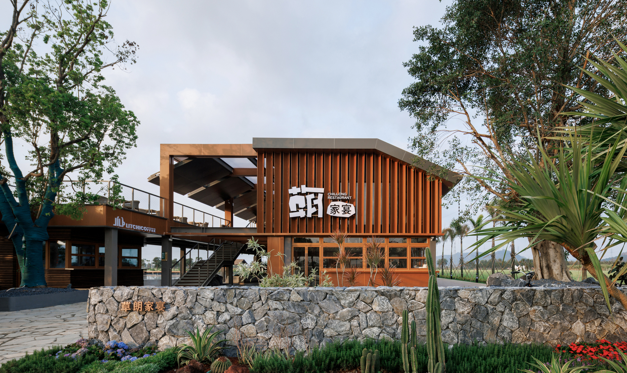 Entrance view of the timber-clad curved roof structure elevated on stone gabion walls with planted beds
