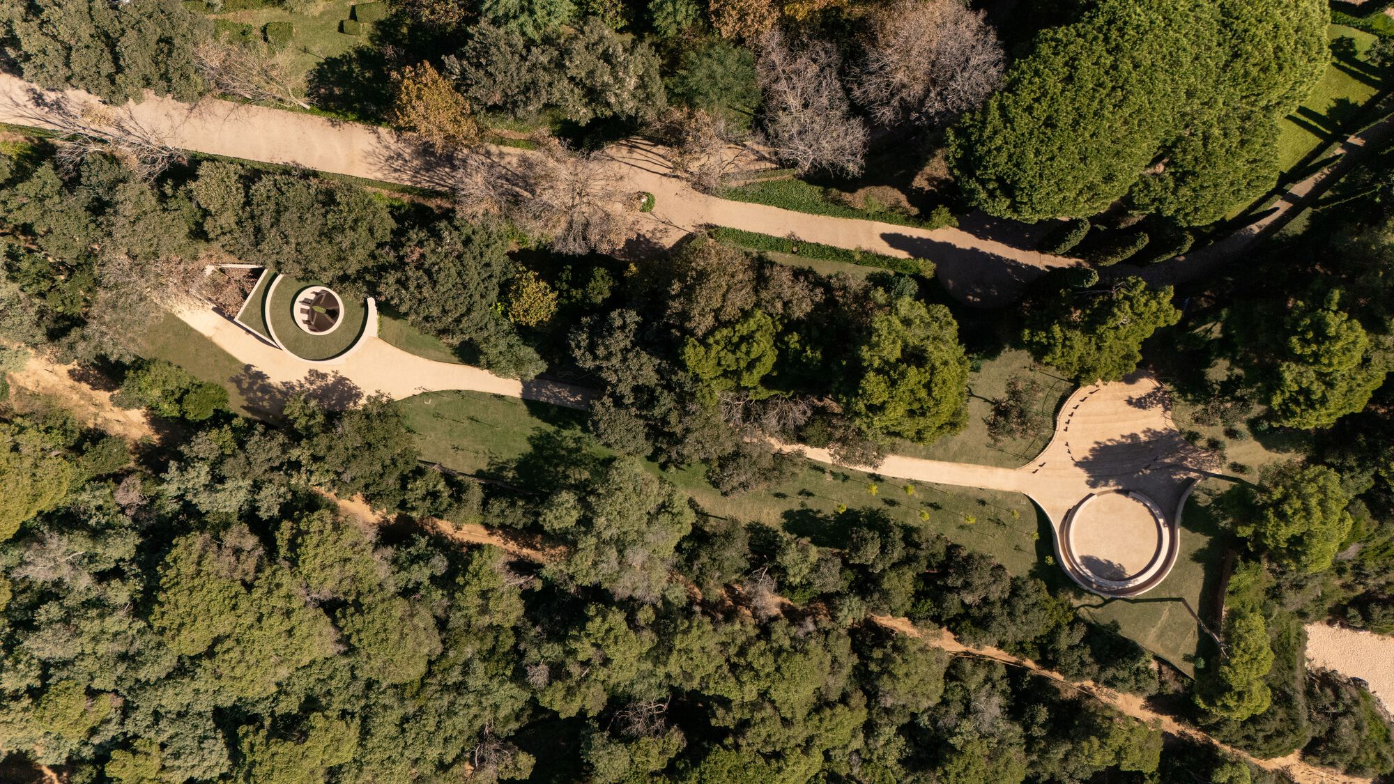Top-down view of two circular pavilions connected by winding pathways through wooded landscape