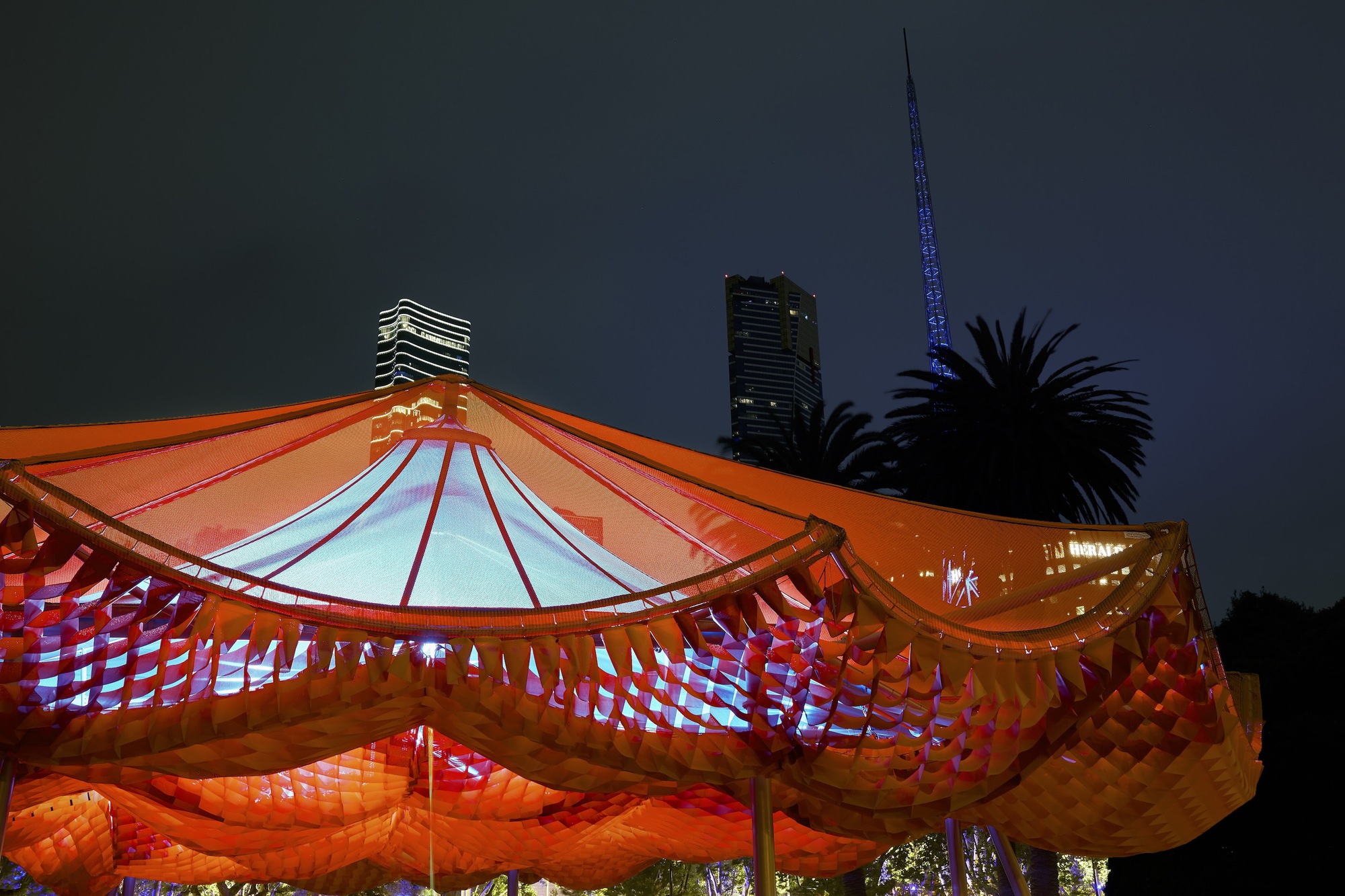 Night view of the illuminated orange canopy with palm trees and towers silhouetted behind