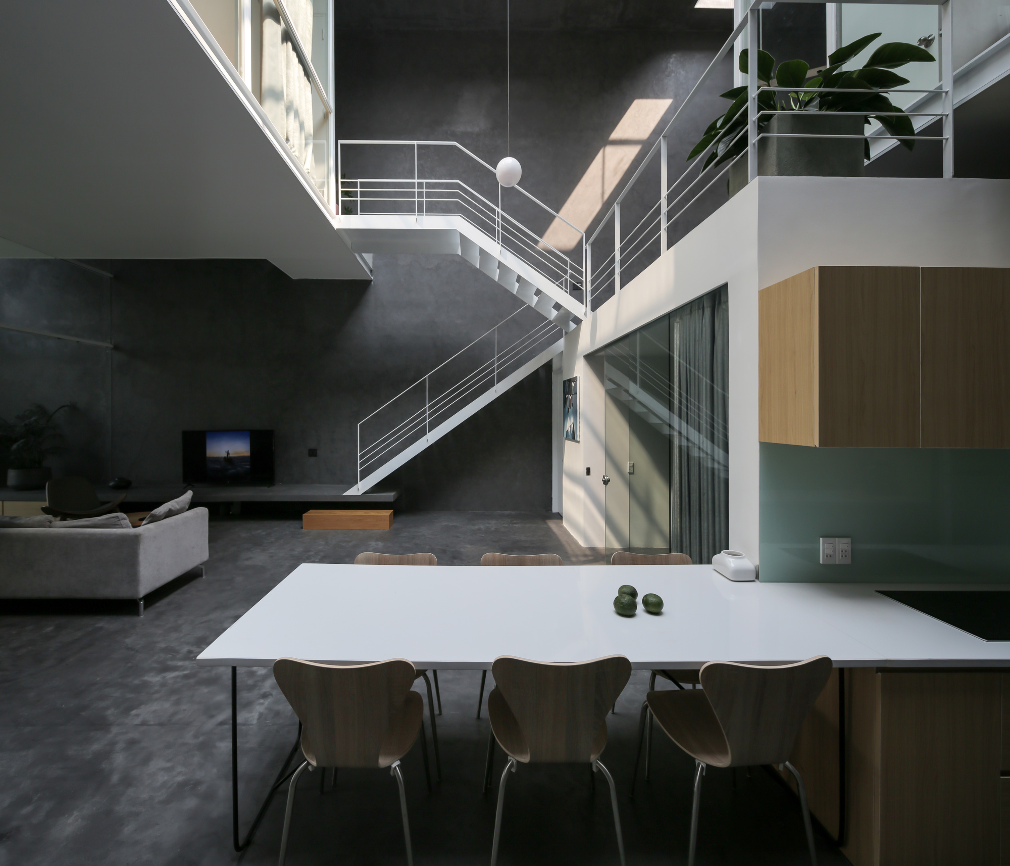 Open-plan dining area with white table beneath steel staircase and double-height concrete walls