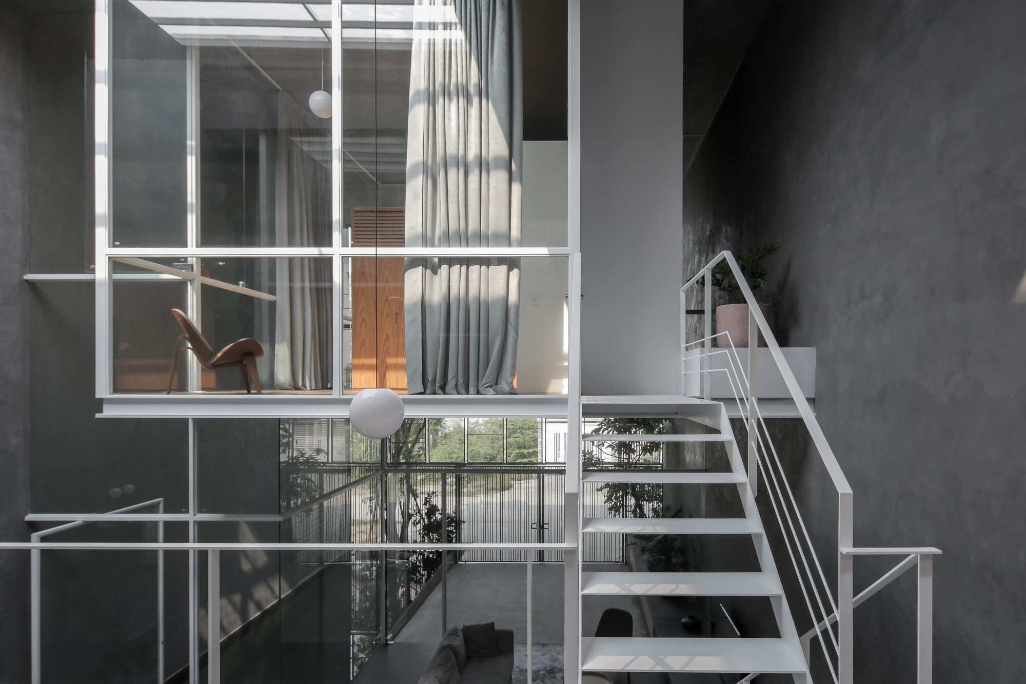 White metal staircase connecting multiple levels beneath a grid skylight with hanging globe lights