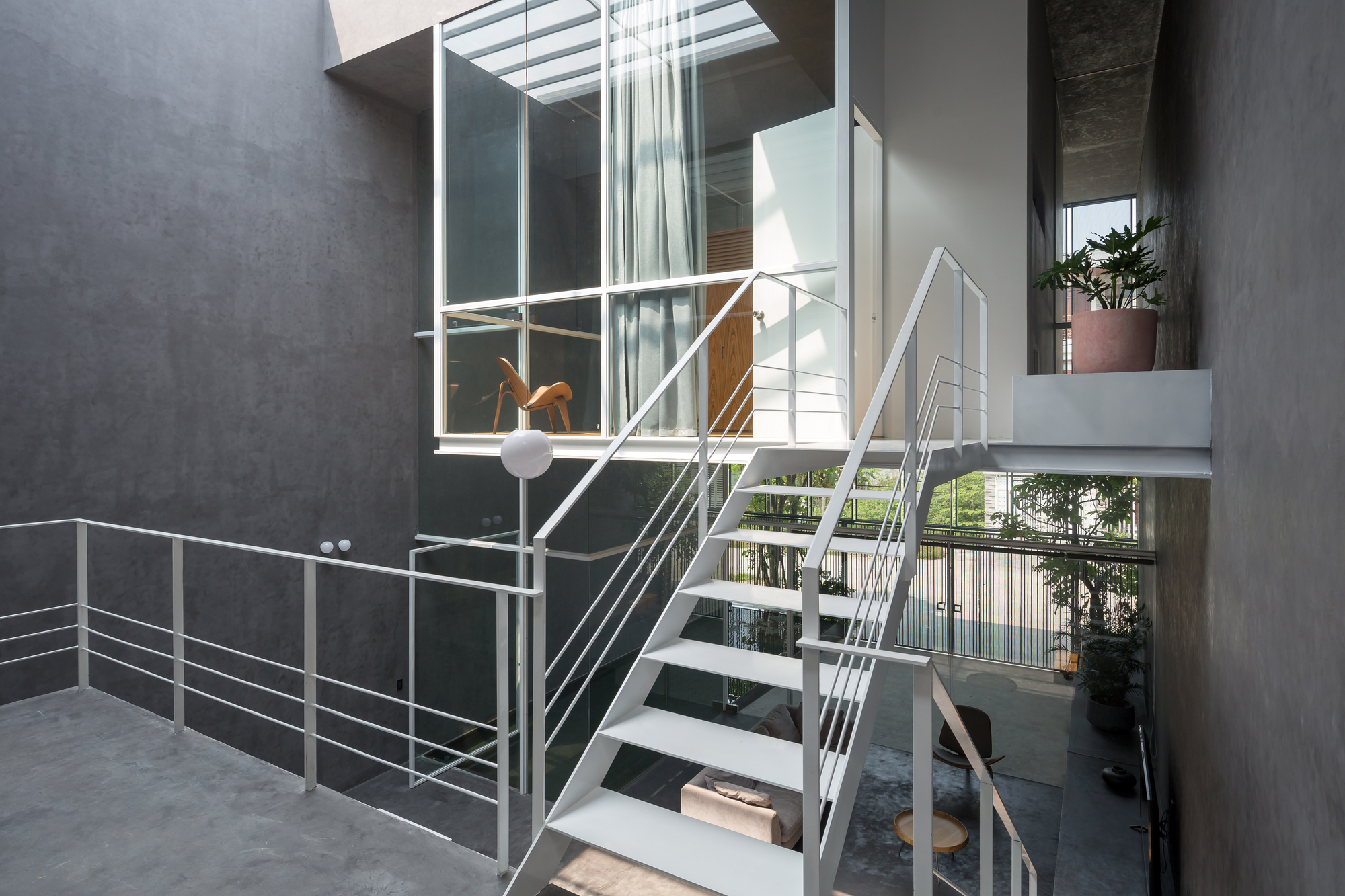 Open-tread steel staircase with cable railings rising through the double-height courtyard space