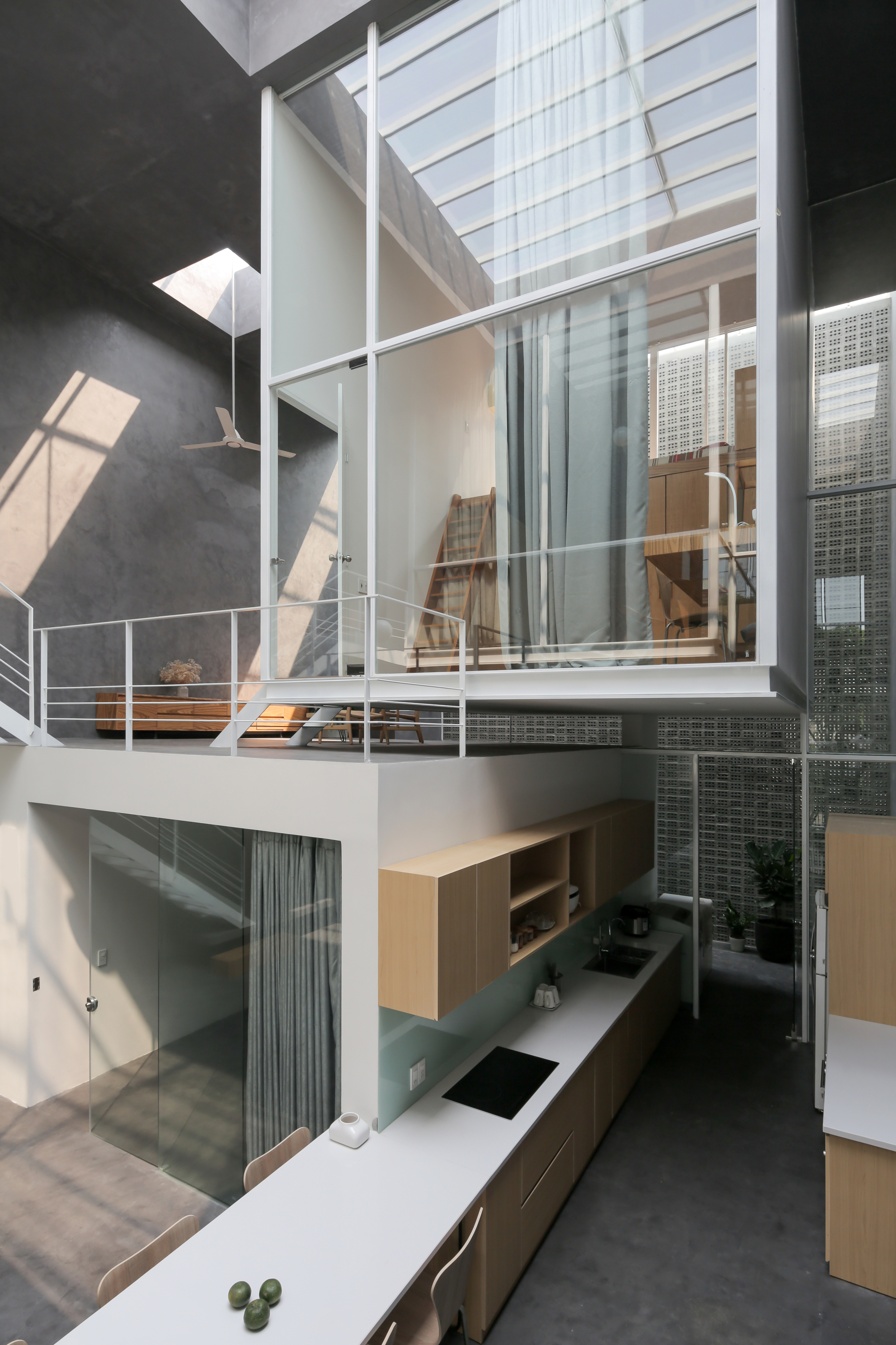 Multi-level interior void showing kitchen counter, stacked volumes with white railings, and glazed skylight filtering natural light overhead