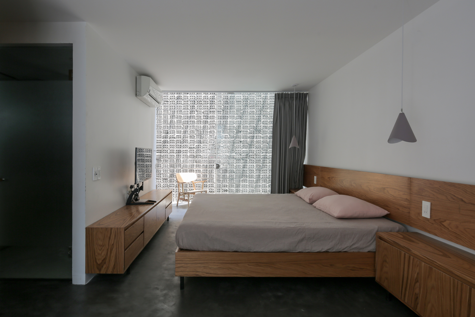 Bedroom with timber platform bed, low credenza, and perforated screen wall filtering daylight through grey curtains