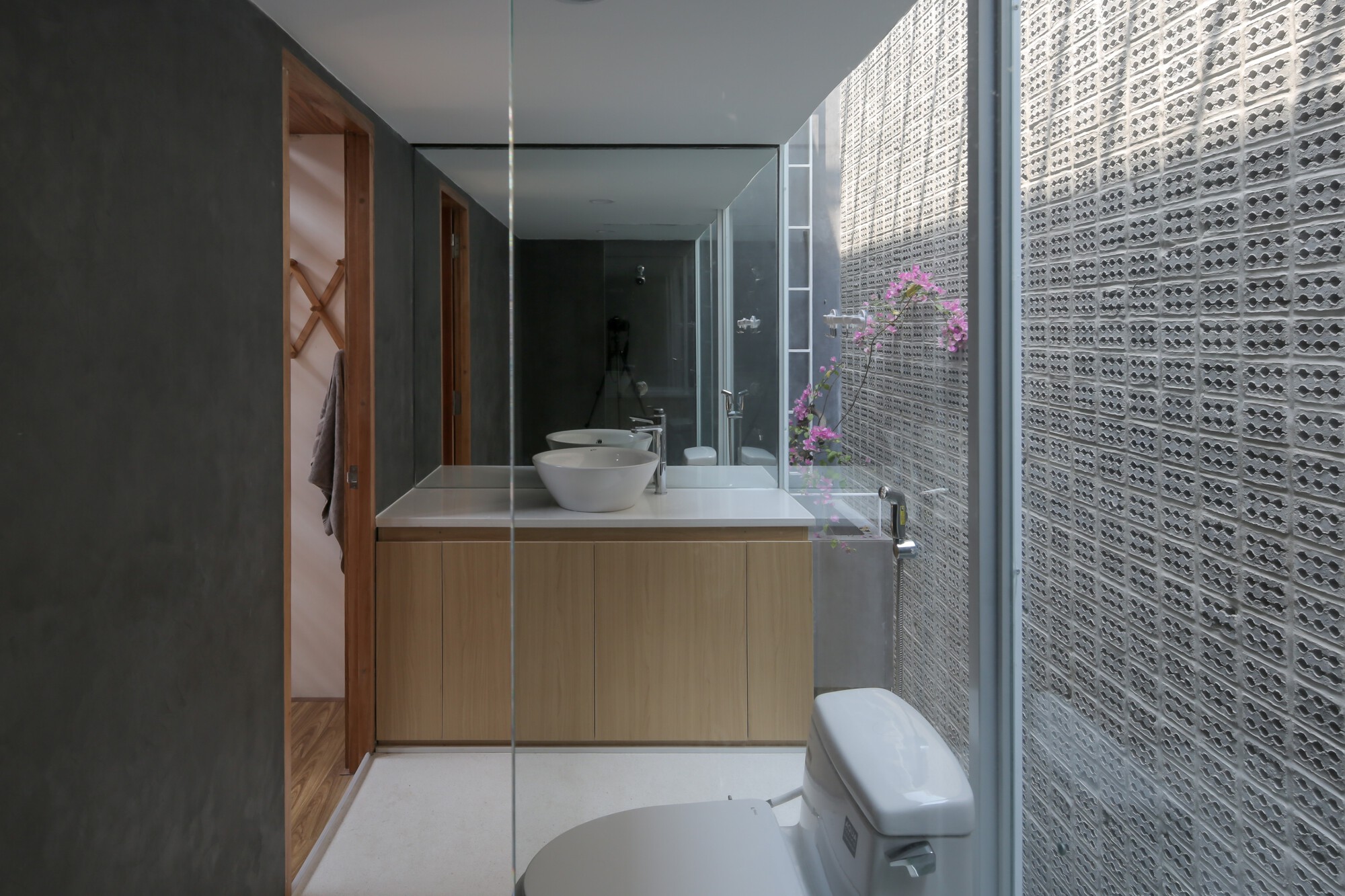 Bathroom vanity with timber cabinetry, mirror, and perforated screen wall opening to planted lightwell with pink flowers