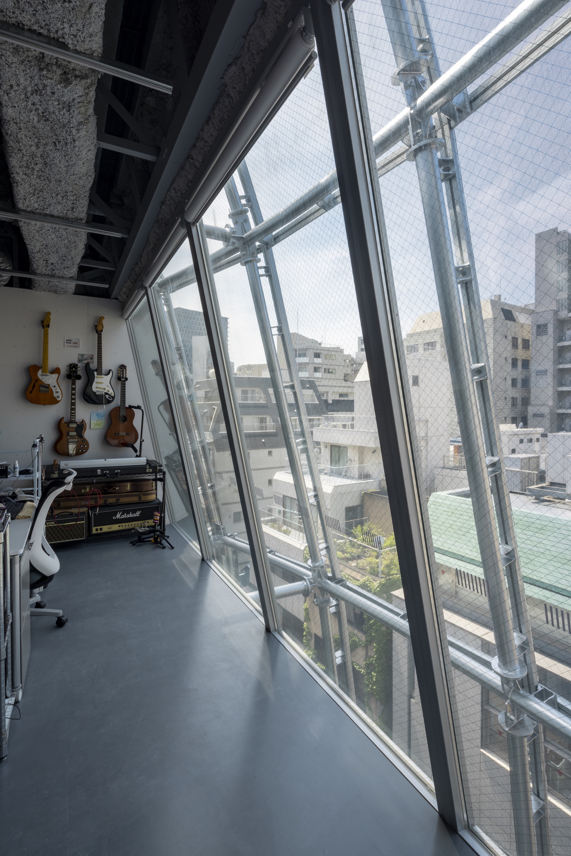 Angled glass curtain wall with visible steel bracing and guitars mounted on the interior wall