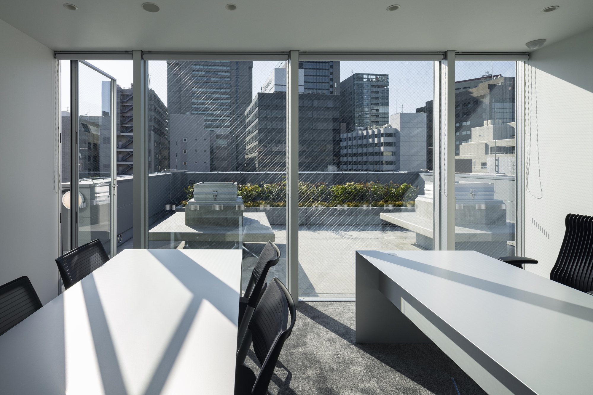 Glazed office space opening to a rooftop terrace with planters and high-rise buildings beyond