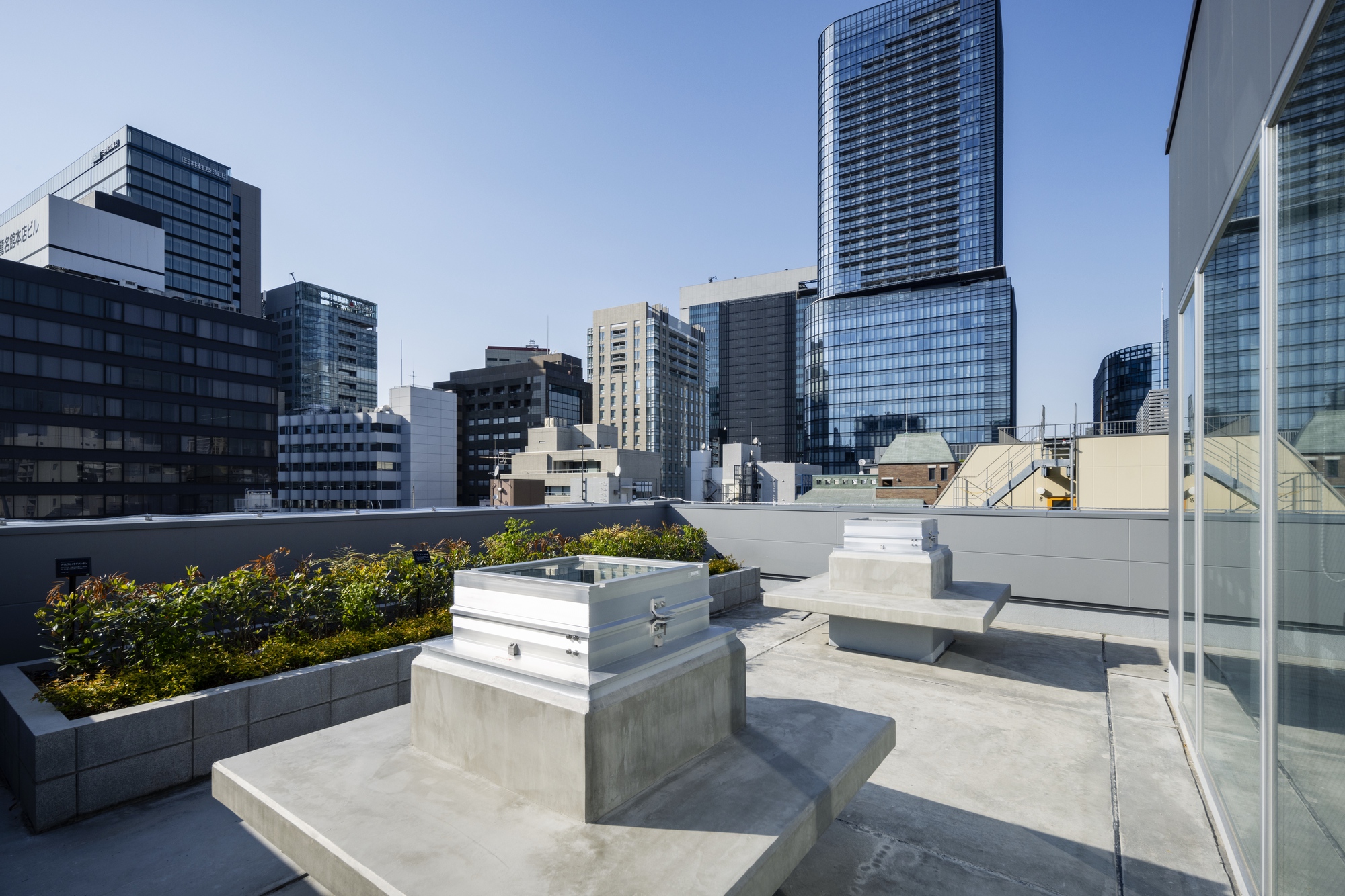 Rooftop terrace with concrete planters, raised garden beds, and stepped seating under clear blue sky