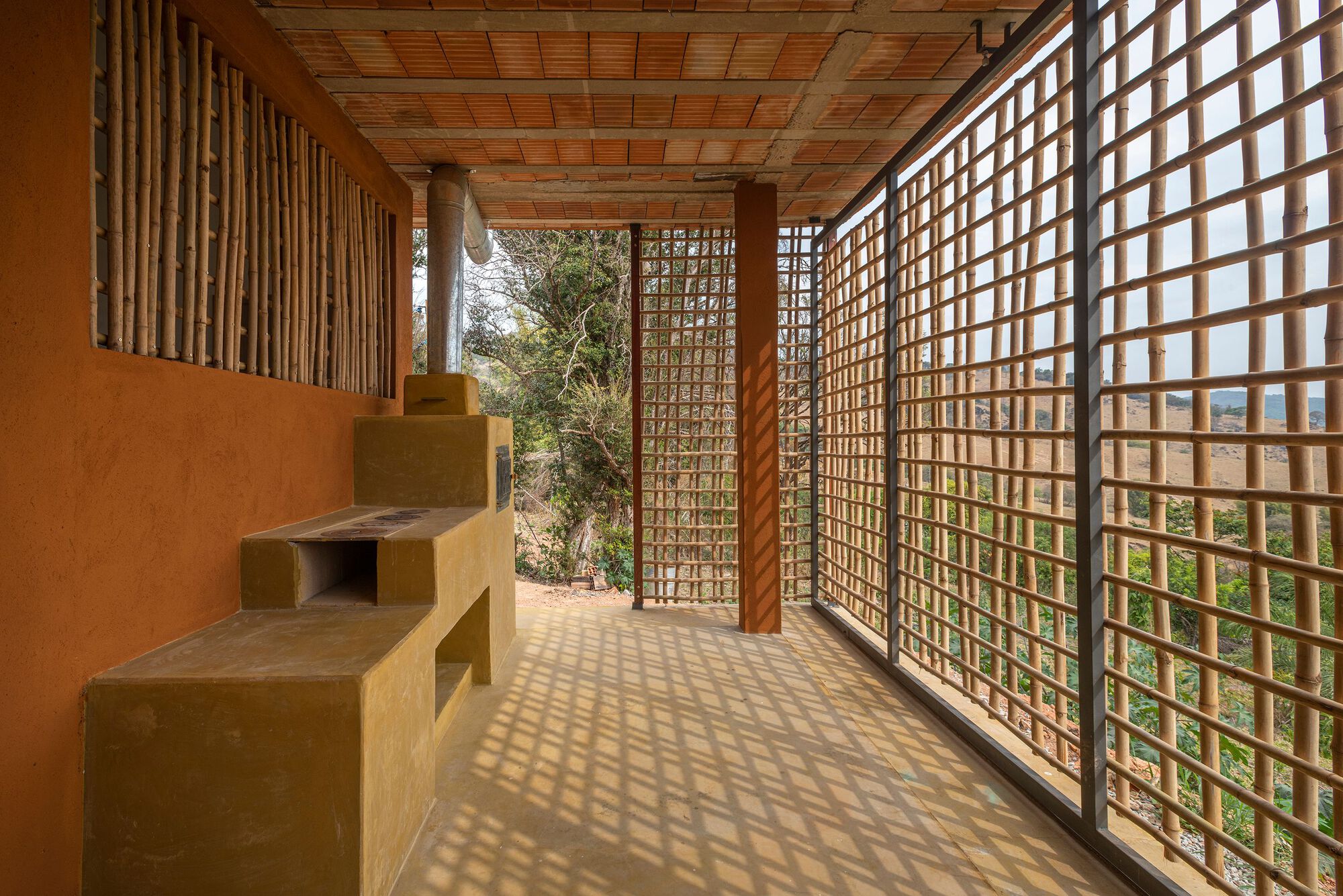 Covered corridor with timber lattice walls casting dappled shadows across the earthen floor and ceiling