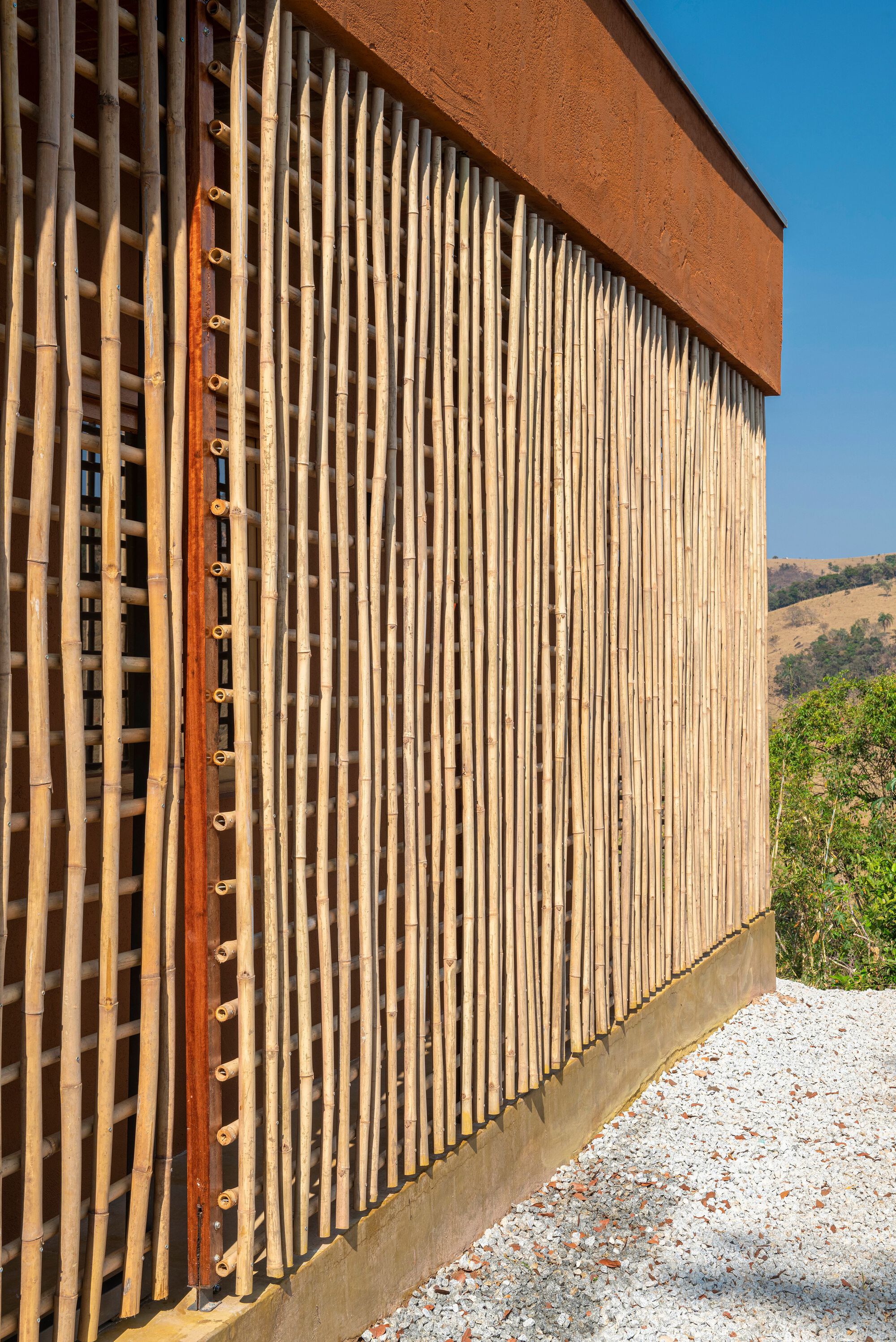 Corner detail of vertical timber louvers with weathered steel gutter against hillside landscape