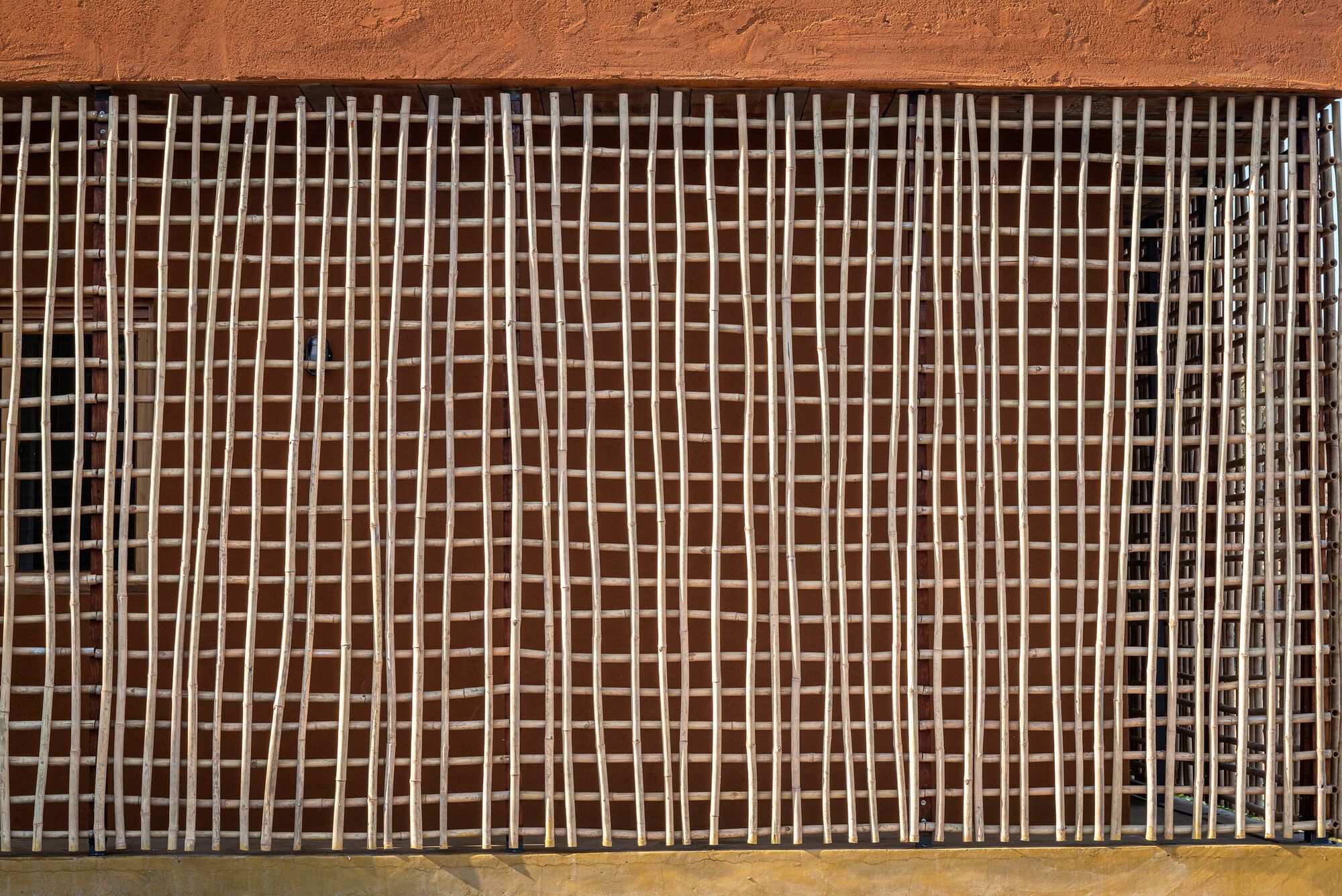 Close-up of the timber lattice screen grid with alternating shadows on earthen wall