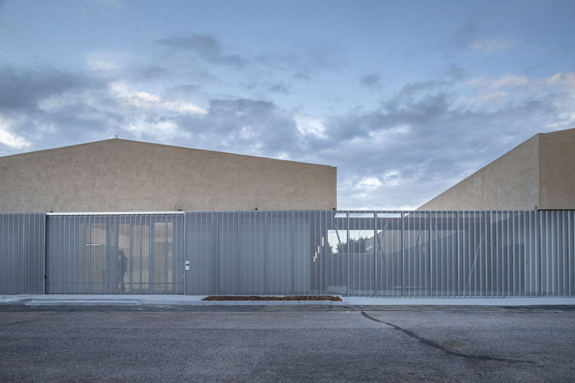 Entrance facade showing glazed openings set within the vertical metal cladding beneath dramatic clouded sky