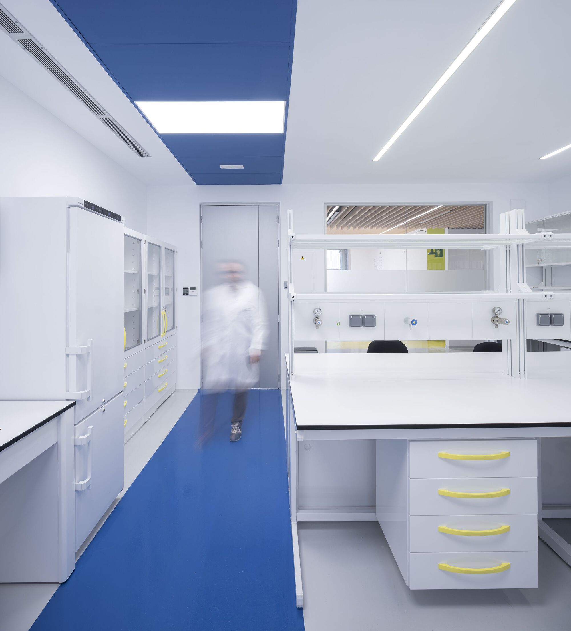 Laboratory interior with white casework and blue resin flooring, one person in motion blur