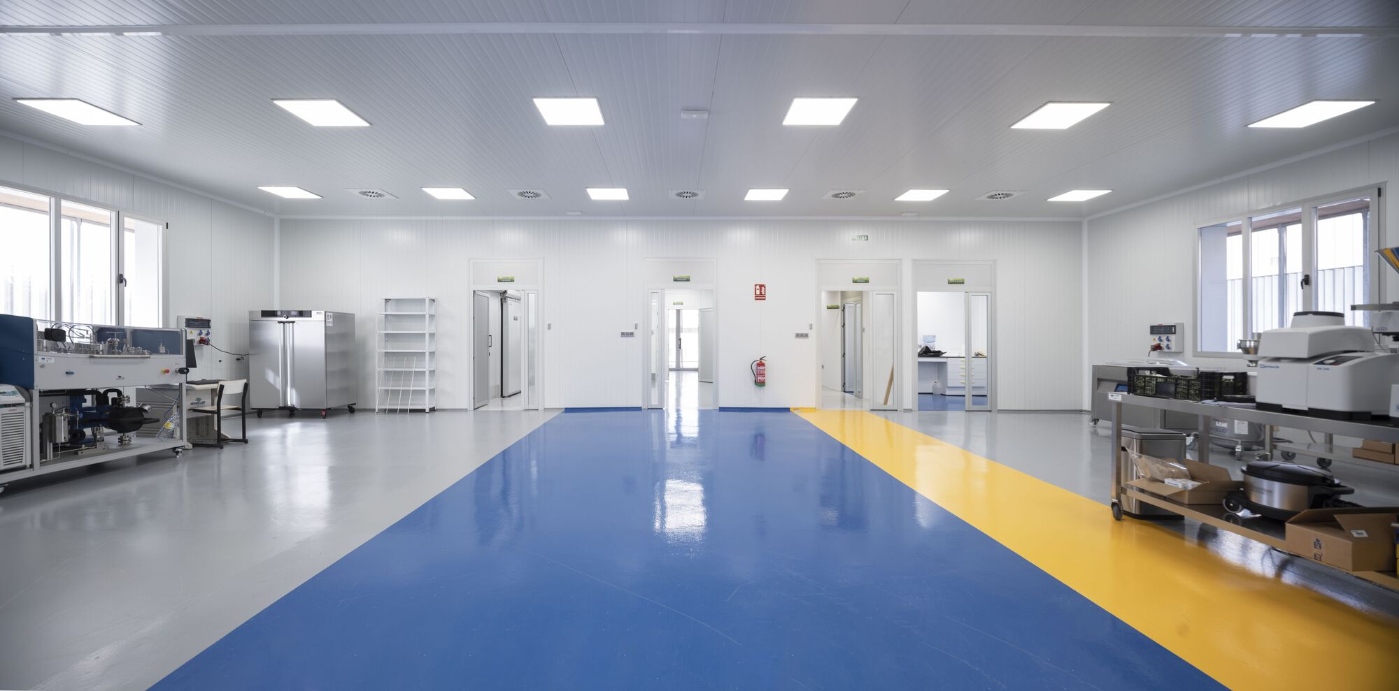 Open laboratory space with blue and yellow floor zones and stainless steel equipment along perimeter