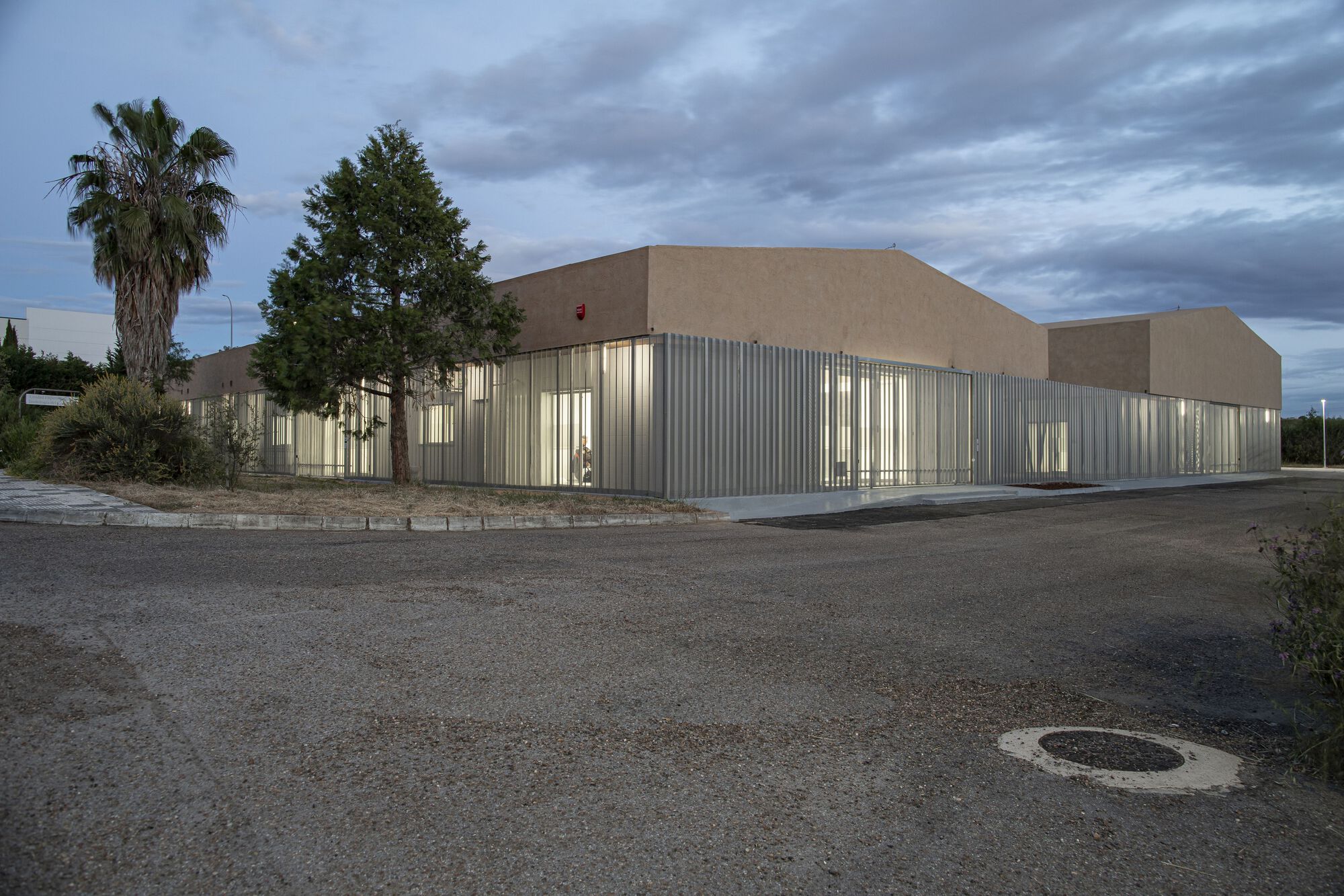 Corner view of the corrugated metal base and stucco upper volume with palm trees at dusk
