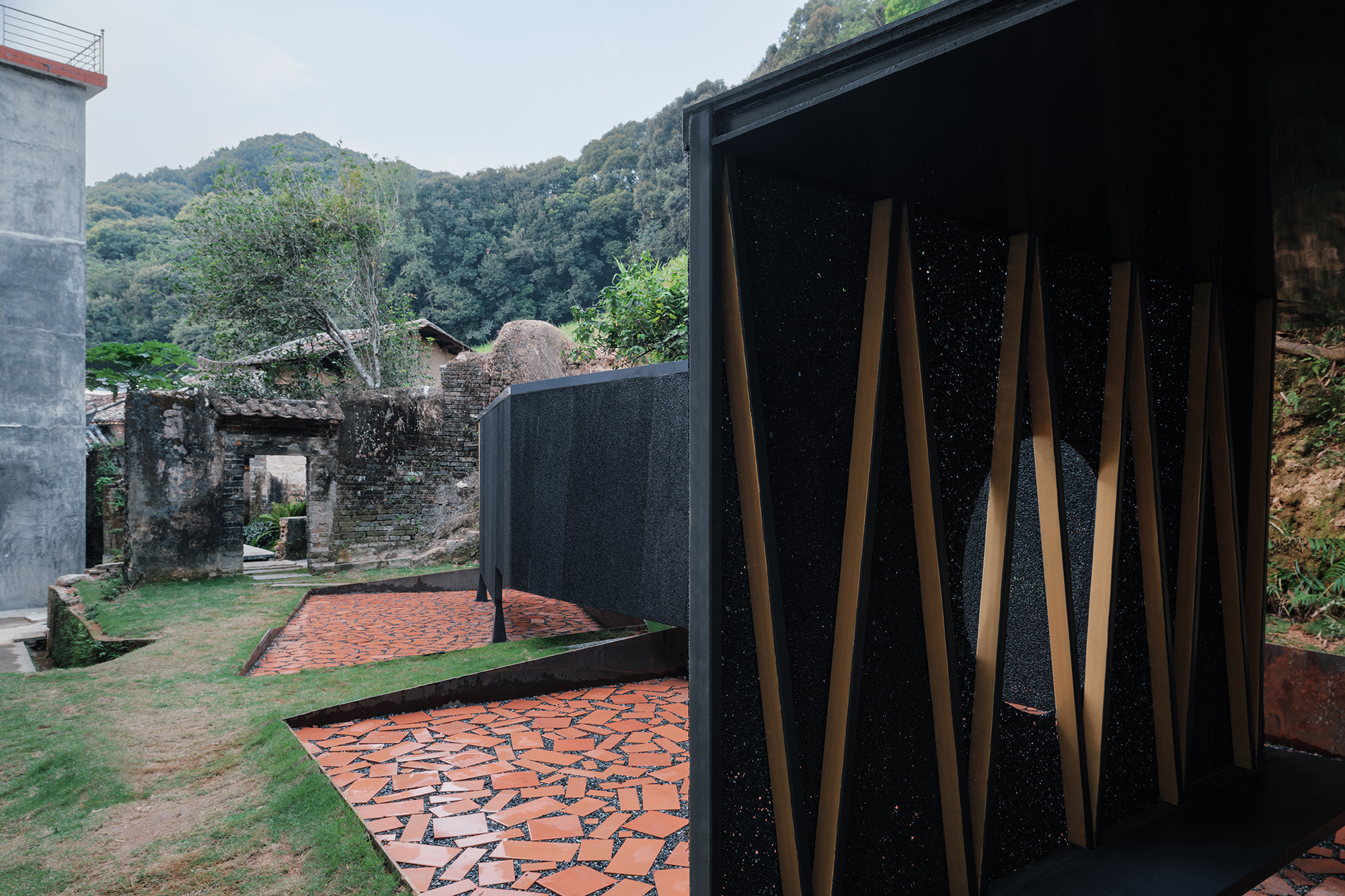 Courtyard with red tile path between ruins and curved black wall with vertical timber slats