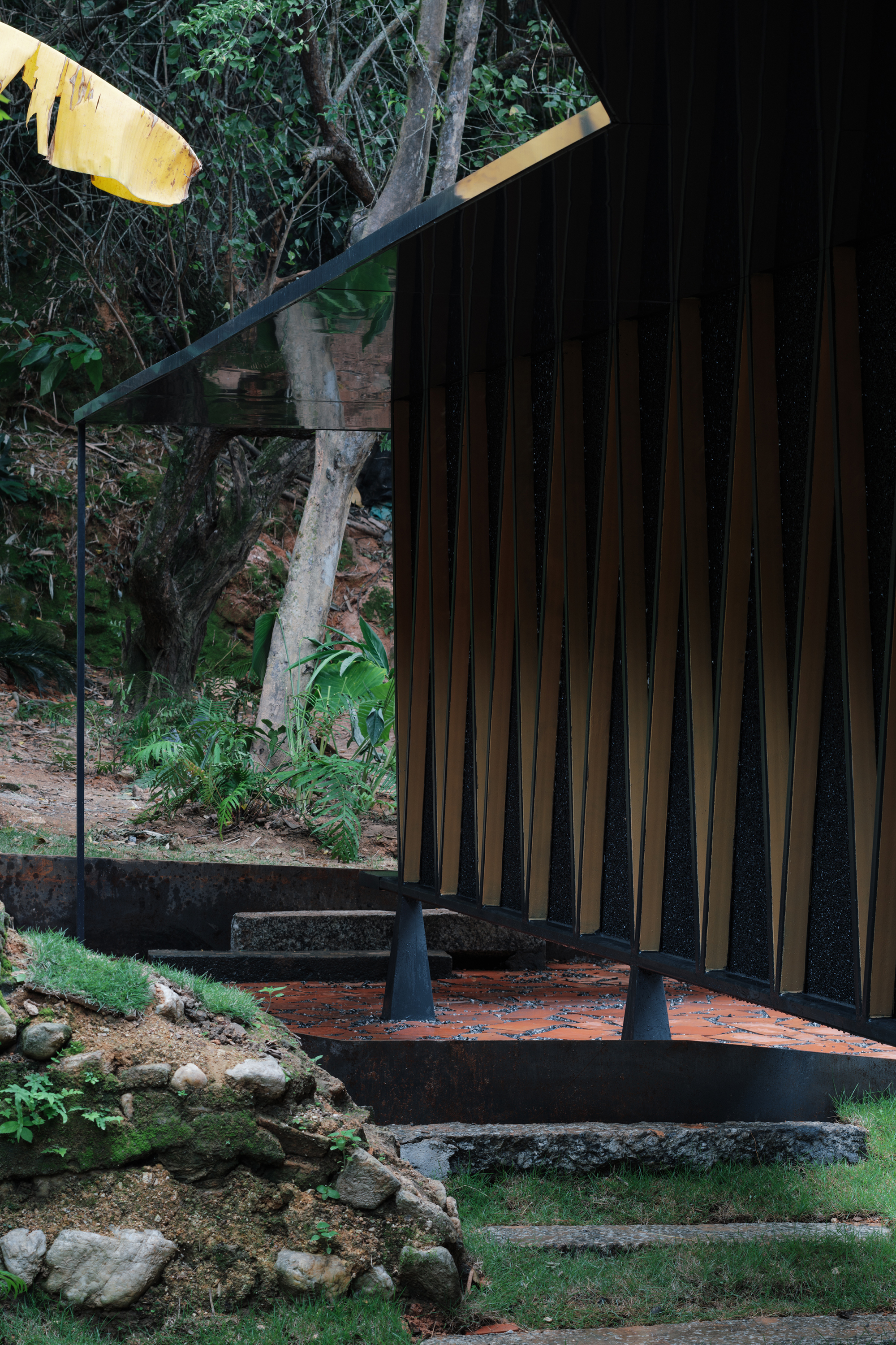 Corner detail showing black support columns and vertical timber slats with hillside vegetation beyond