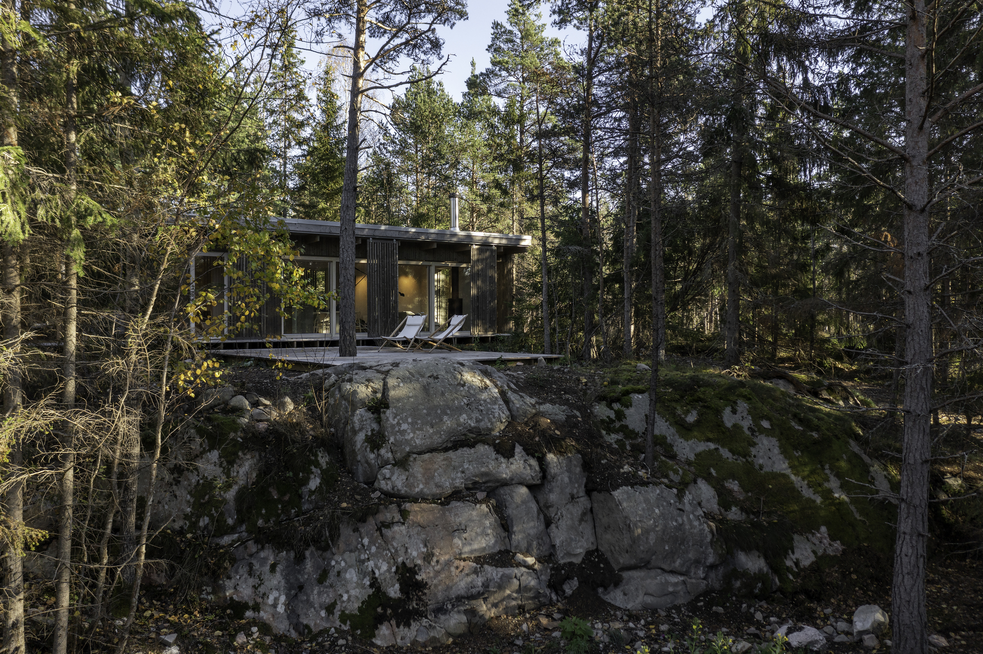 Elevated timber cabin perched on a glacial rock outcrop surrounded by pine forest