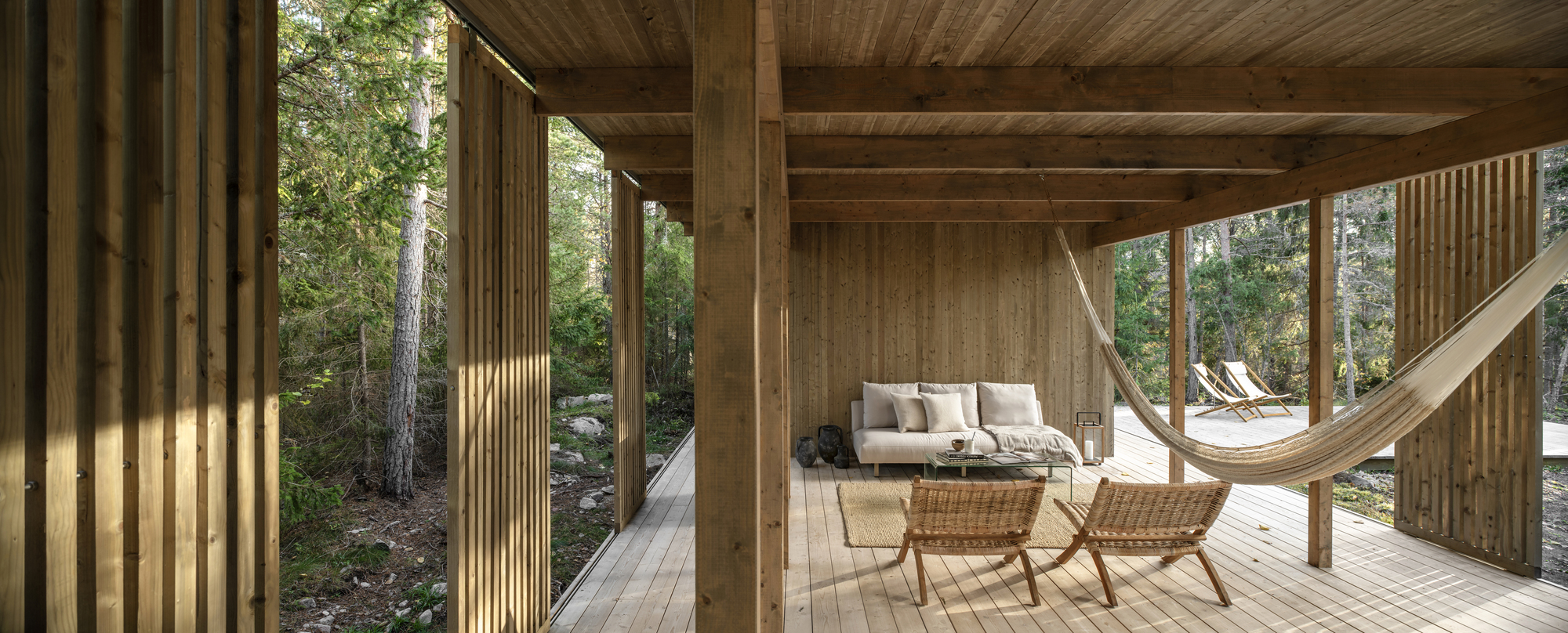 Covered porch with timber columns, plank ceiling and hammock opening to the forest