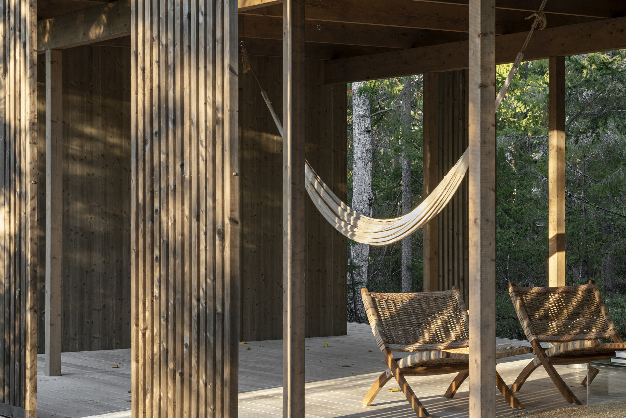 Vertical timber slat screen framing a hammock and folding chairs on an open porch at dusk