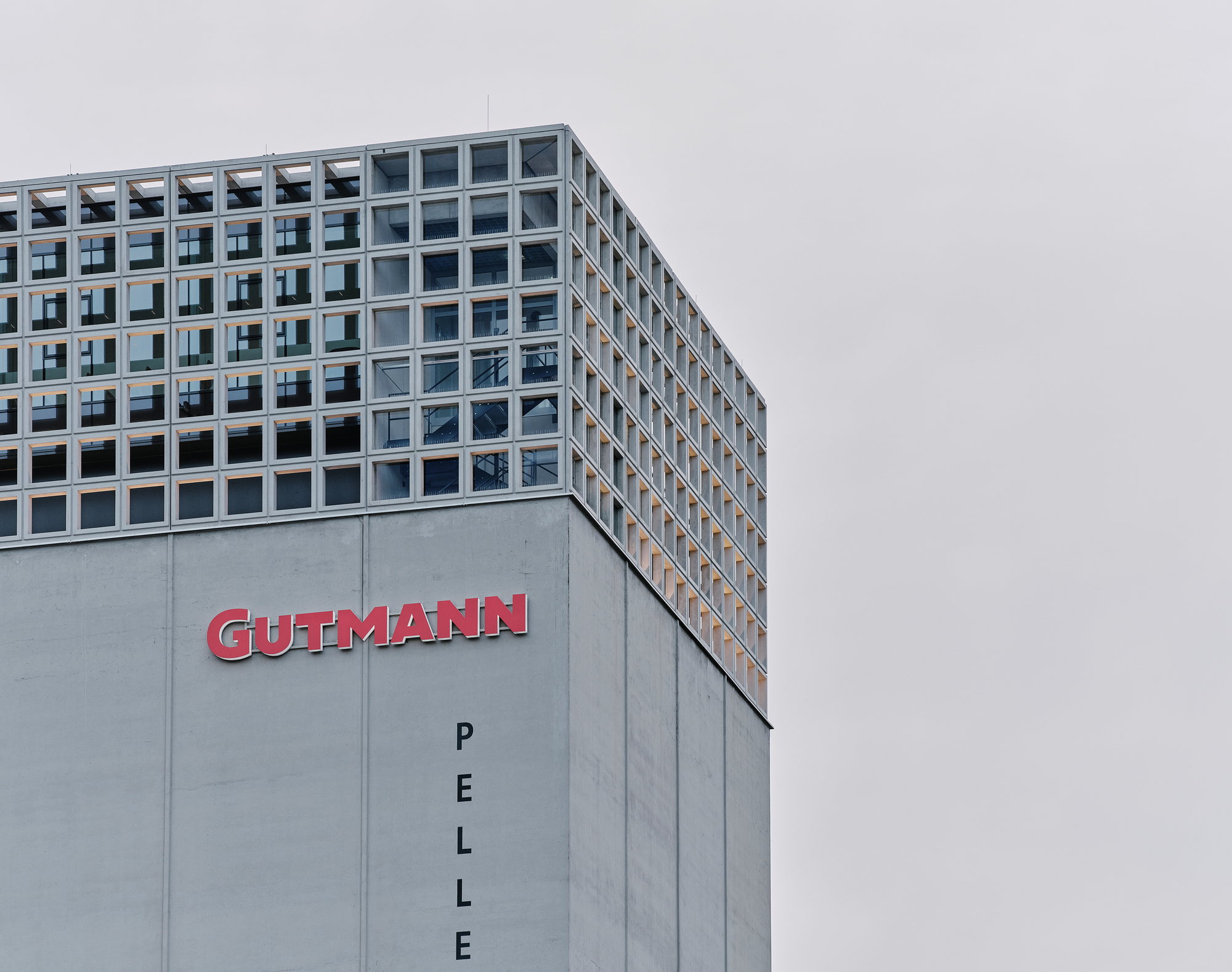 Corner view of the concrete podium and gridded glass facade above under an overcast sky