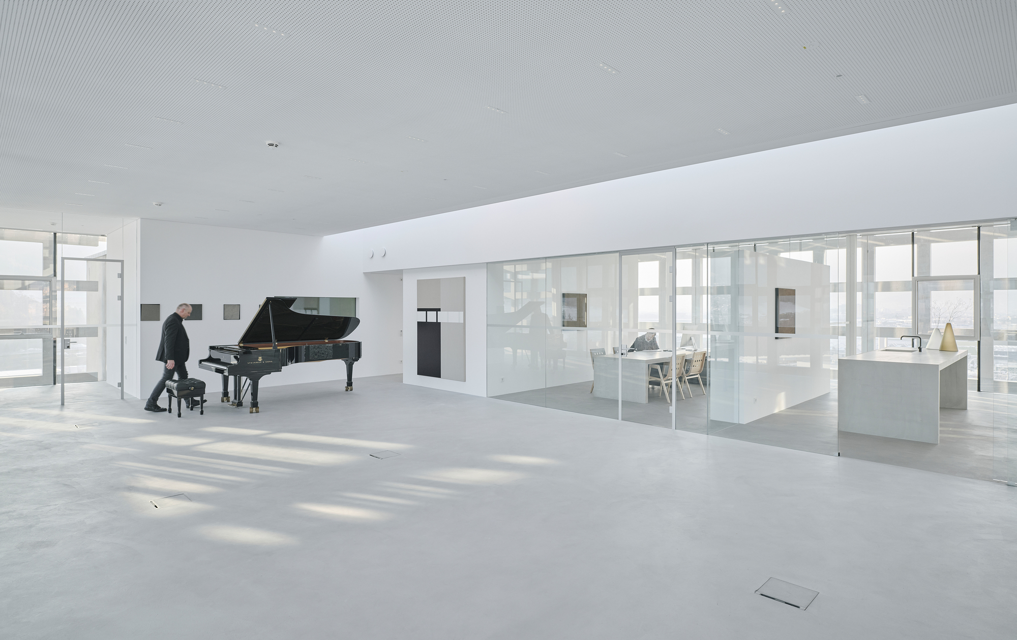 White terrazzo floor and glass-walled room with a person seated at the piano by the windows