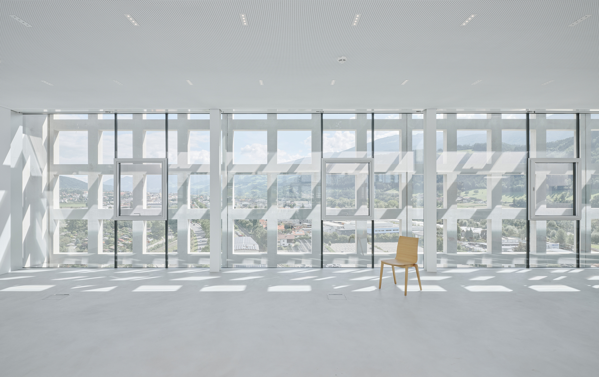 Single wooden chair facing the perforated white screen wall and full-height glazing beyond