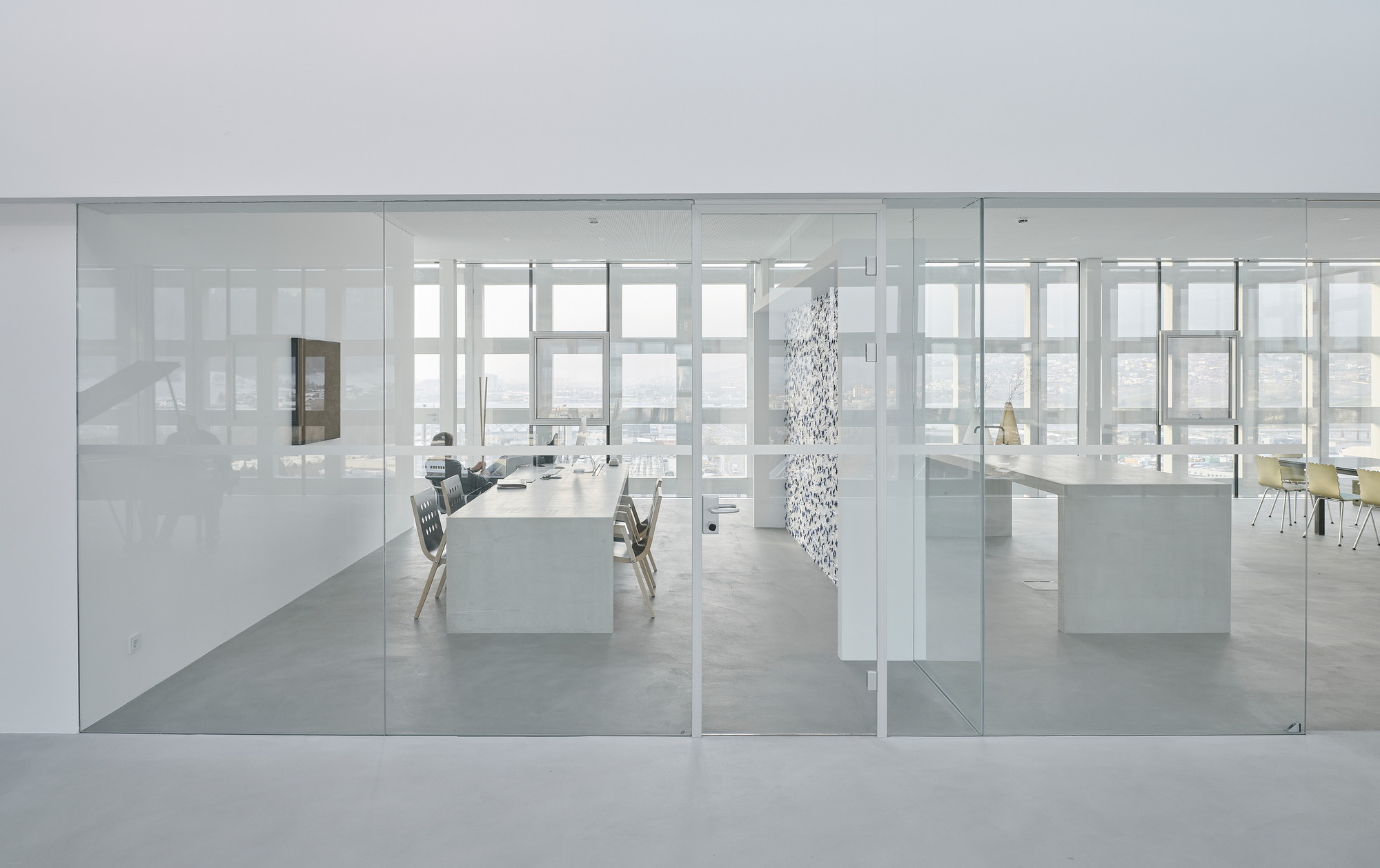 View through frameless glass partitions into the white workspace with pendant light and distant windows