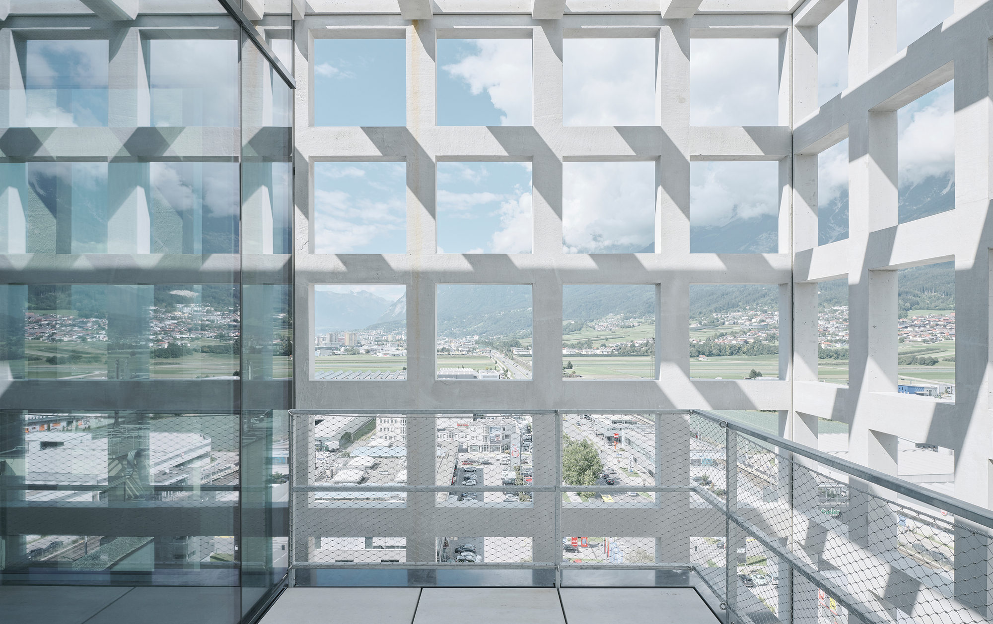 Geometric white sun screen casting patterned shadows across a glass-floored balcony with valley views
