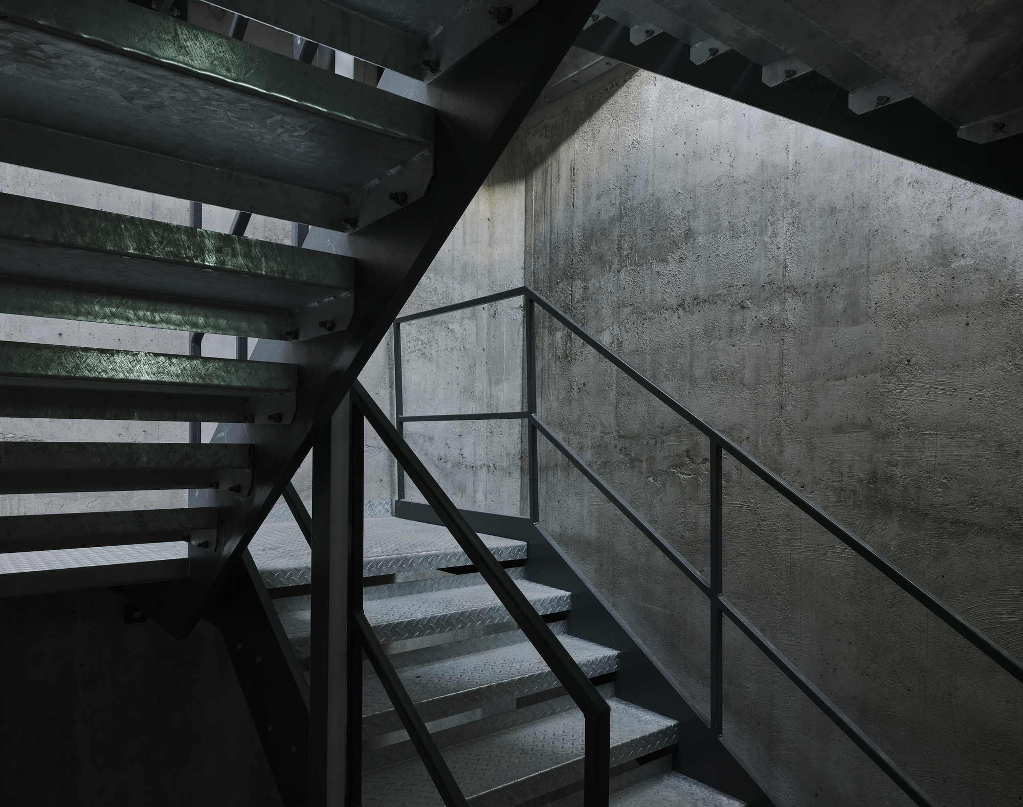 Metal staircase with perforated treads against board-formed concrete wall in shadowed stairwell