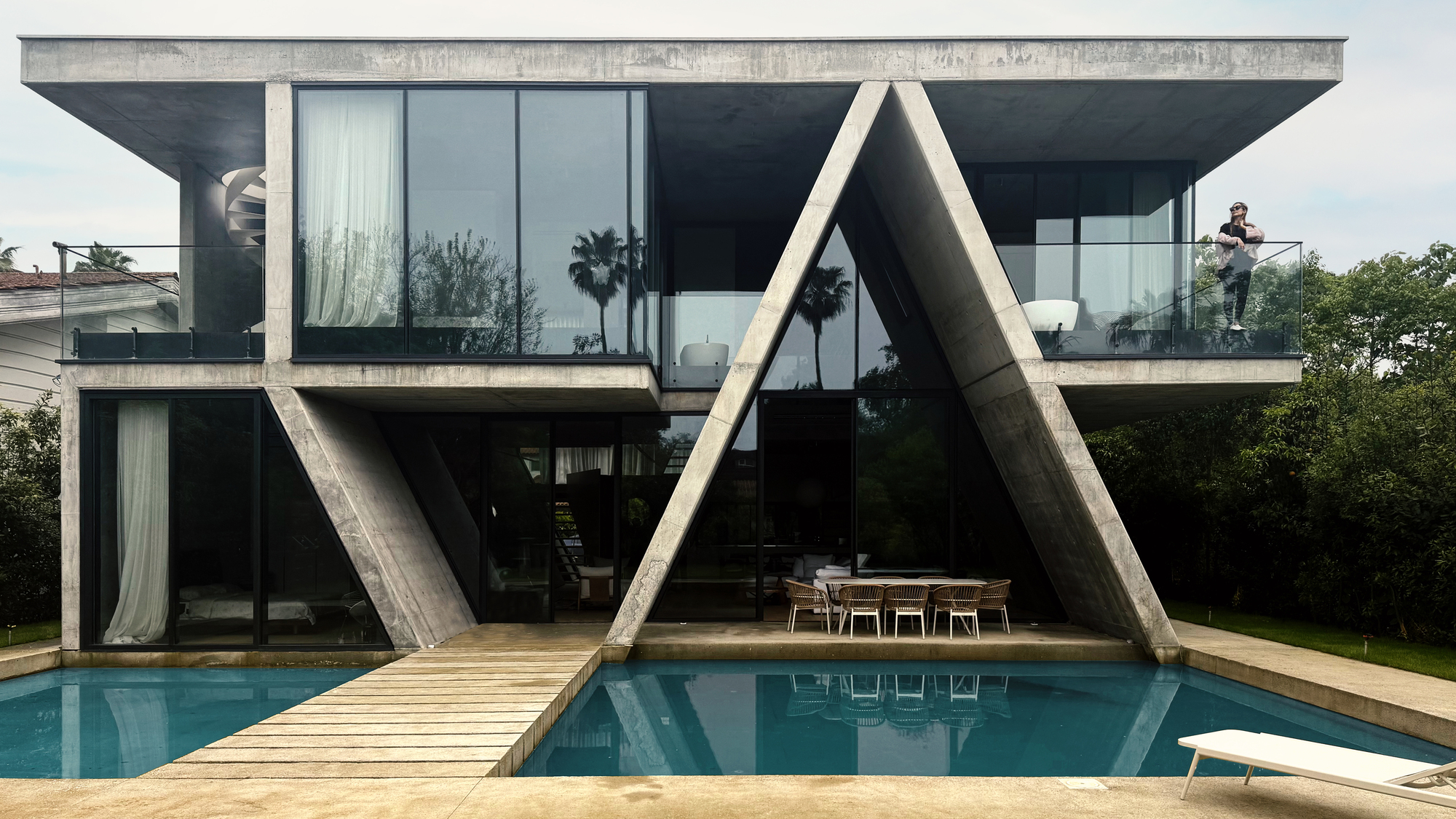 Rear elevation showing the angled concrete columns reflected in the swimming pool with timber bridge crossing water