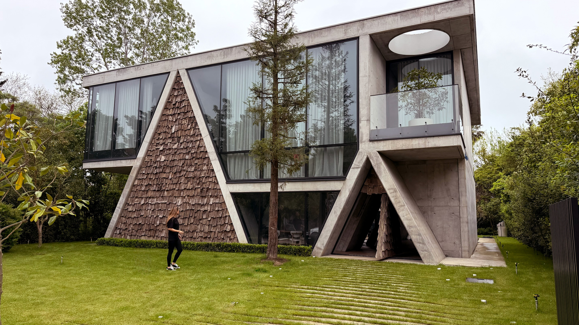 Side view of the triangular textured volume and diagonal concrete supports with a person walking on lawn