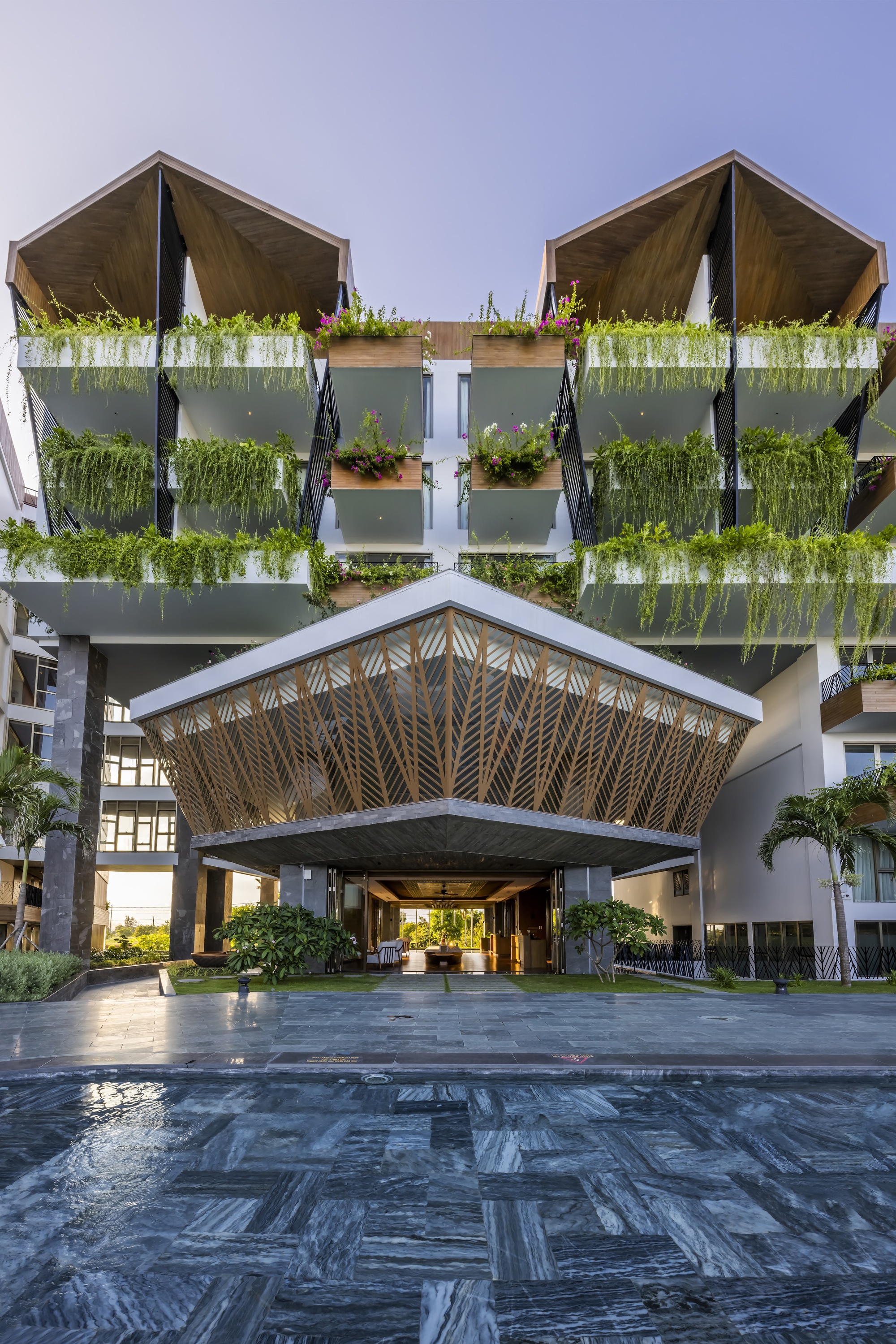 Entrance canopy with woven bamboo ceiling pattern above dark paving and reflecting pool at dusk