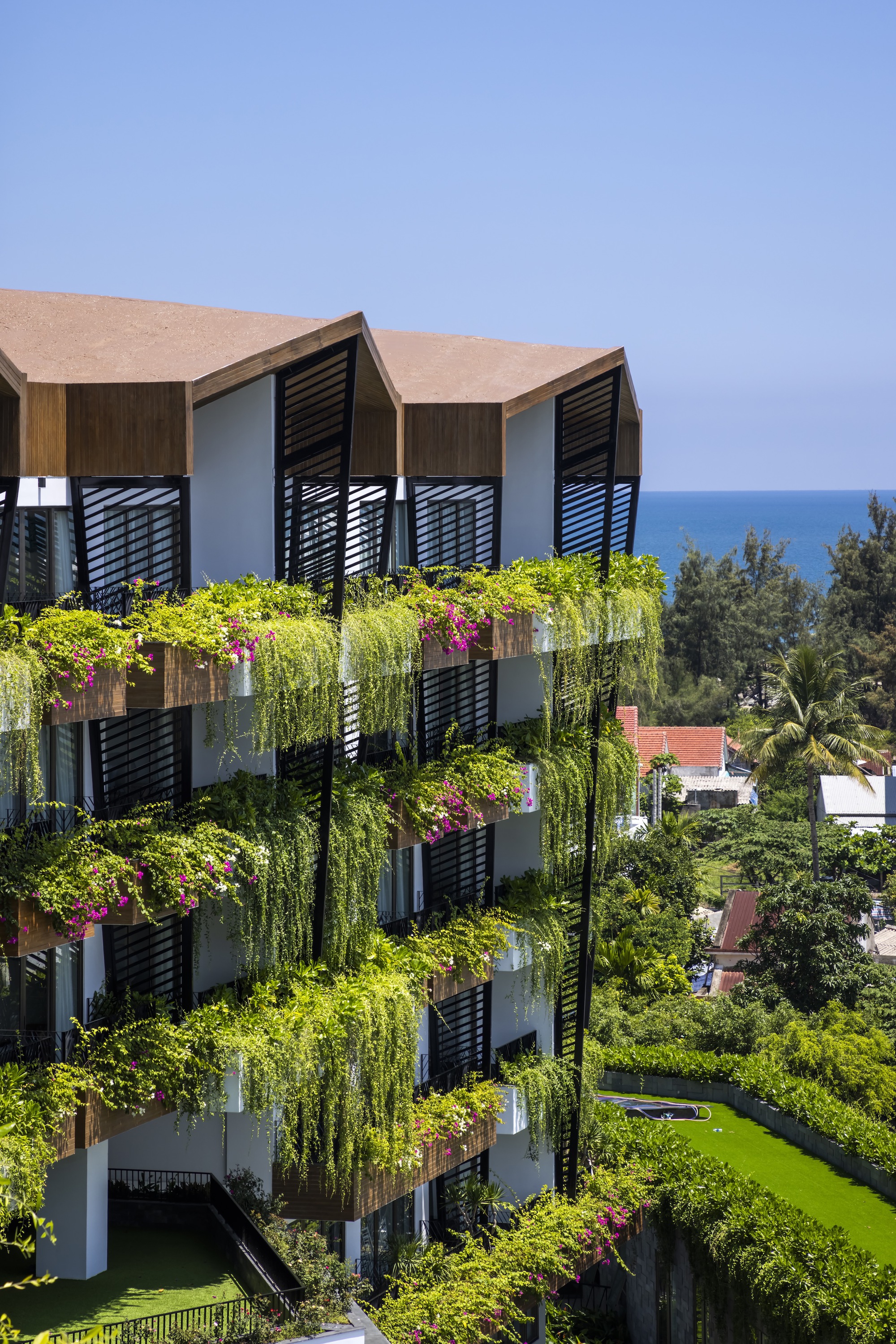 Corner elevation showing zigzag balconies with timber cladding and planted boxes with ocean in the distance