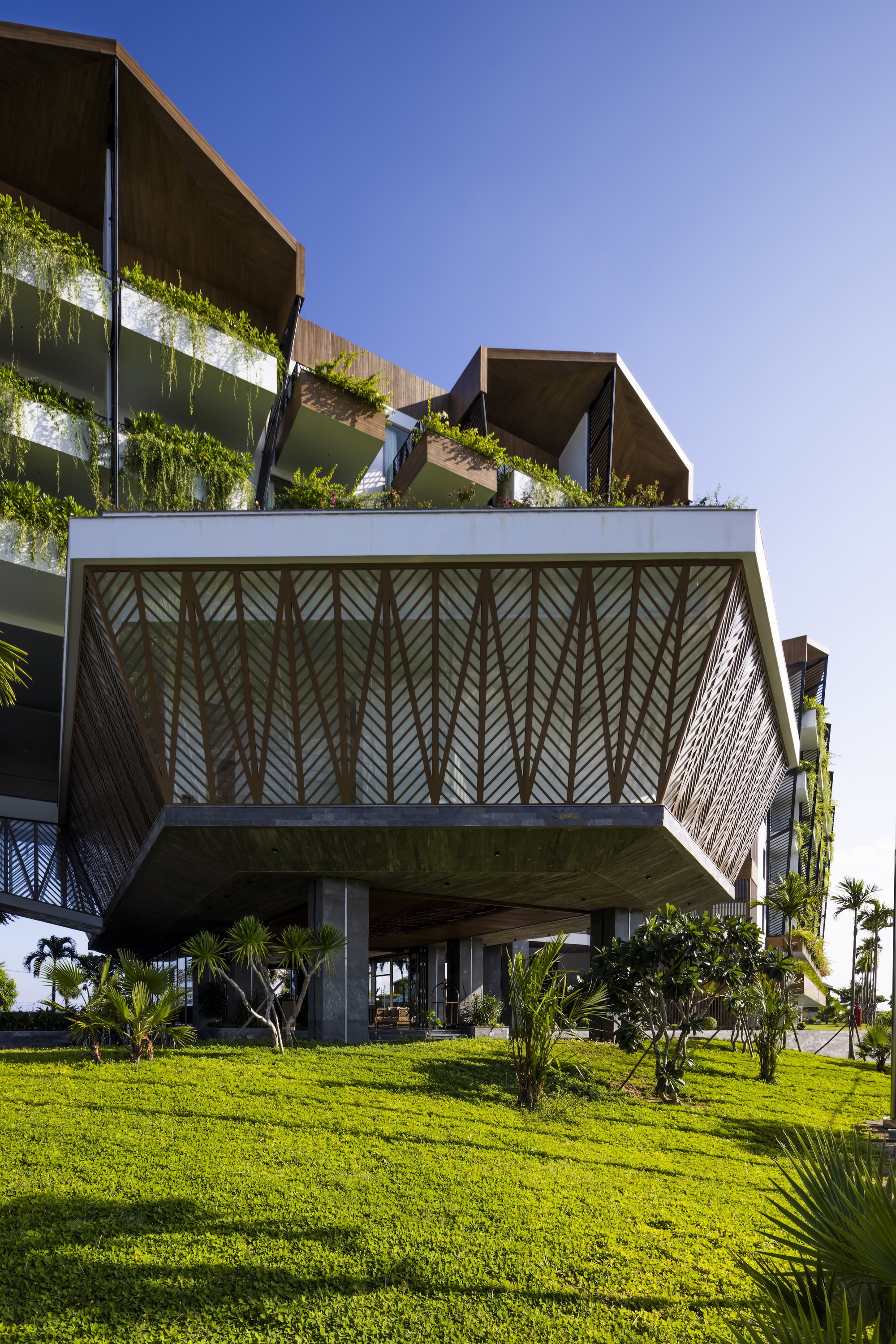 Cantilevered upper floor with herringbone timber screens suspended above a grass lawn and palm trees