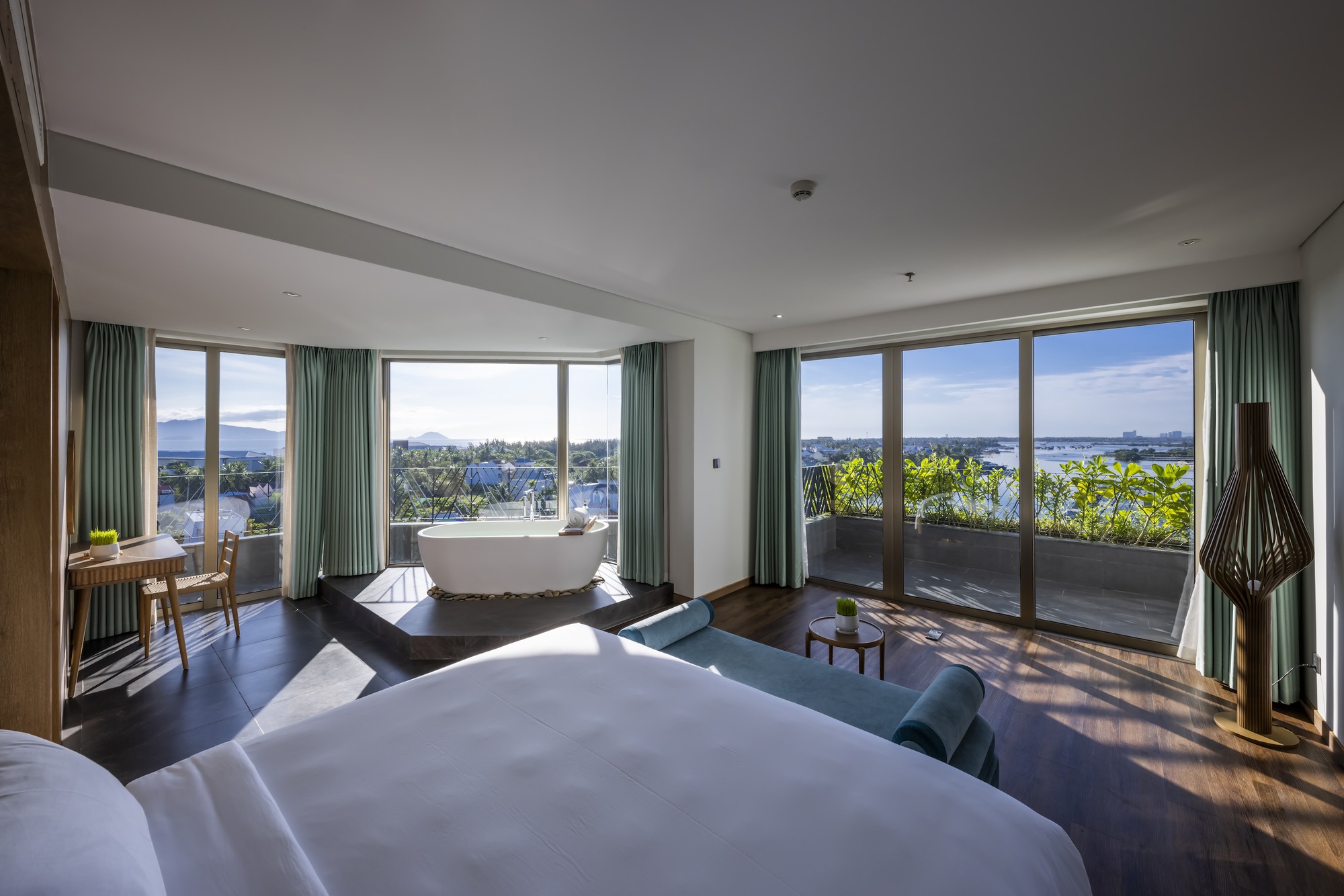 Hotel bedroom with floor-to-ceiling windows opening to a planted balcony with mountain views