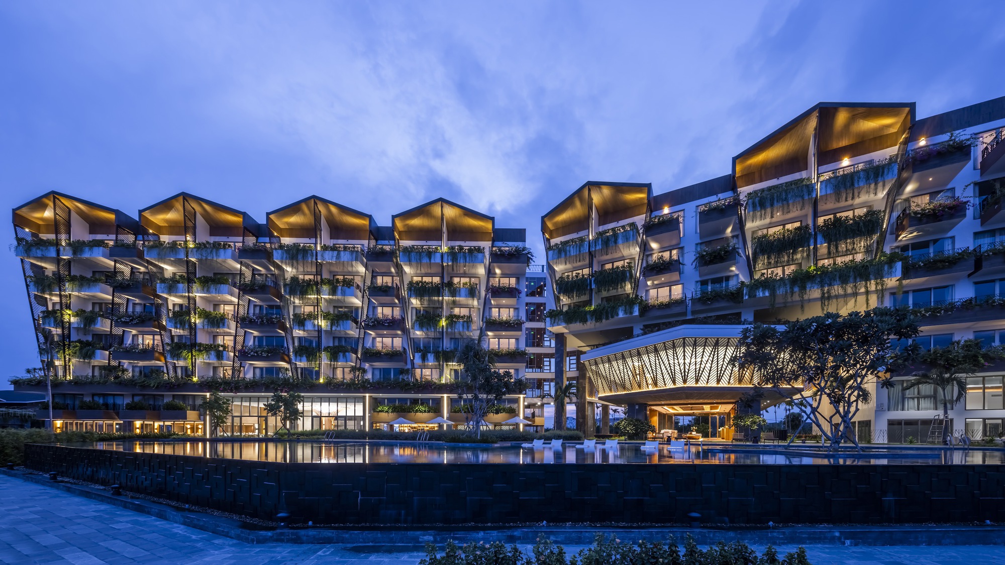 Waterfront facade with stacked balconies, cantilevered pavilions and illuminated chevron screen canopy at dusk