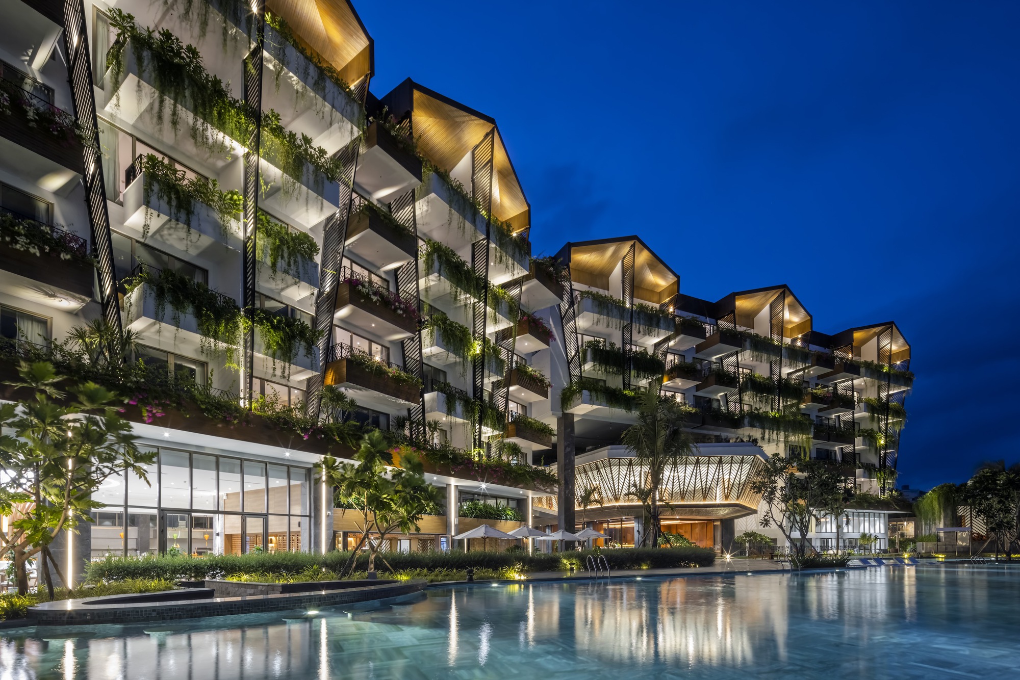 Residential tower facade with planted balconies and illuminated overhangs reflected in the pool at dusk