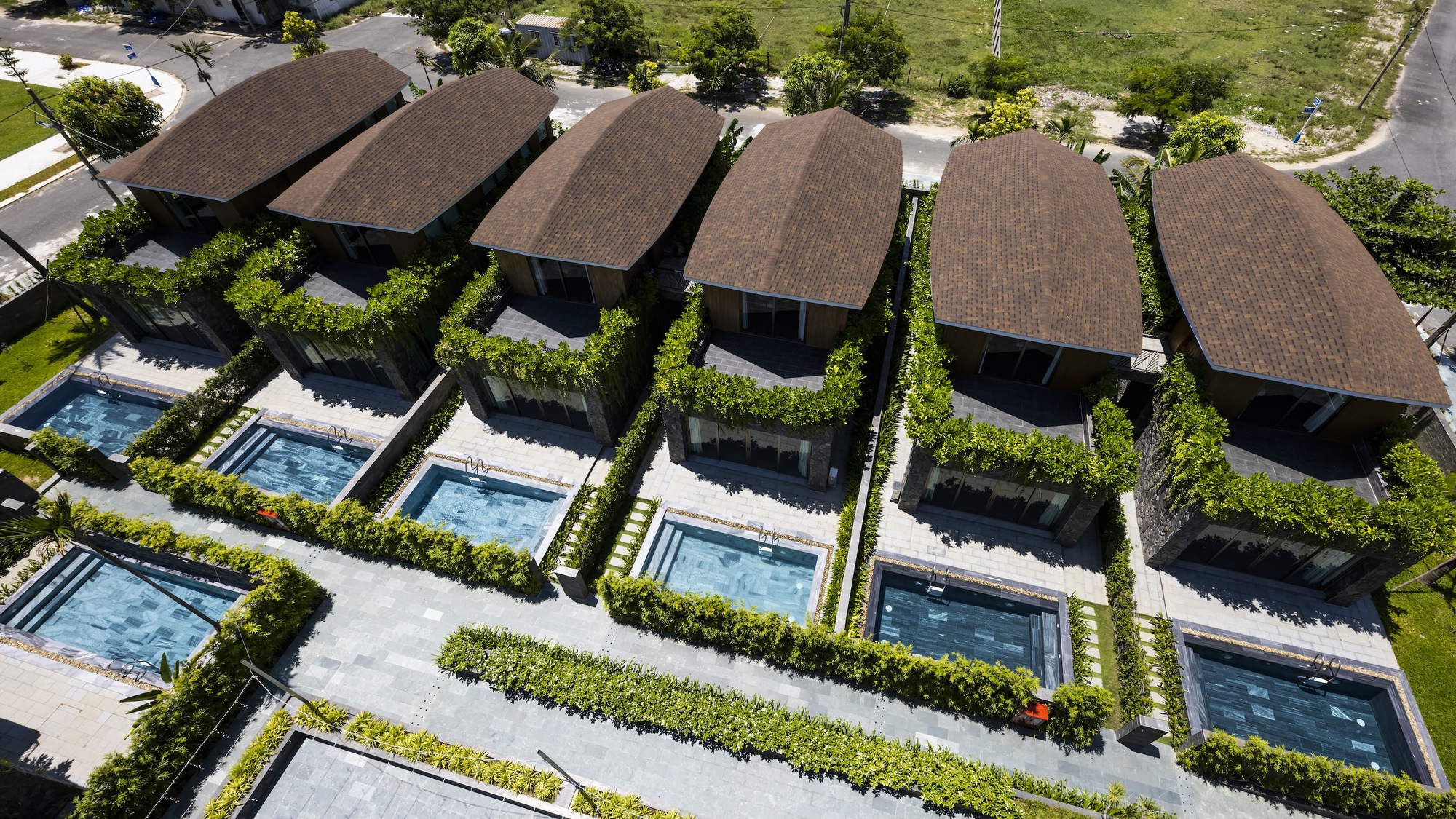 Aerial view of five villas with curved roofs arranged in a row beside individual pools