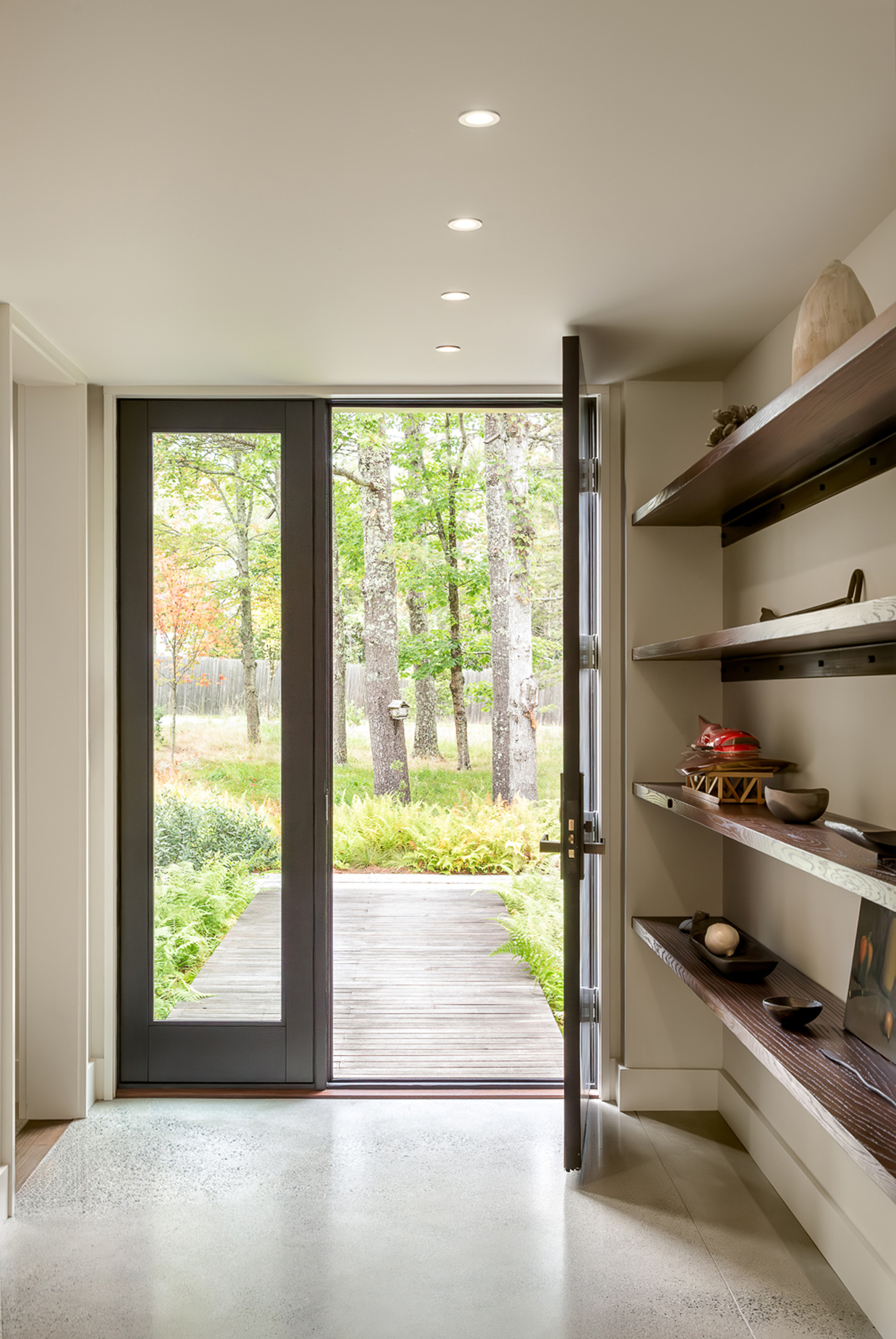 Entry hall with glazed door opening to a timber boardwalk through the forest and timber shelving along one wall
