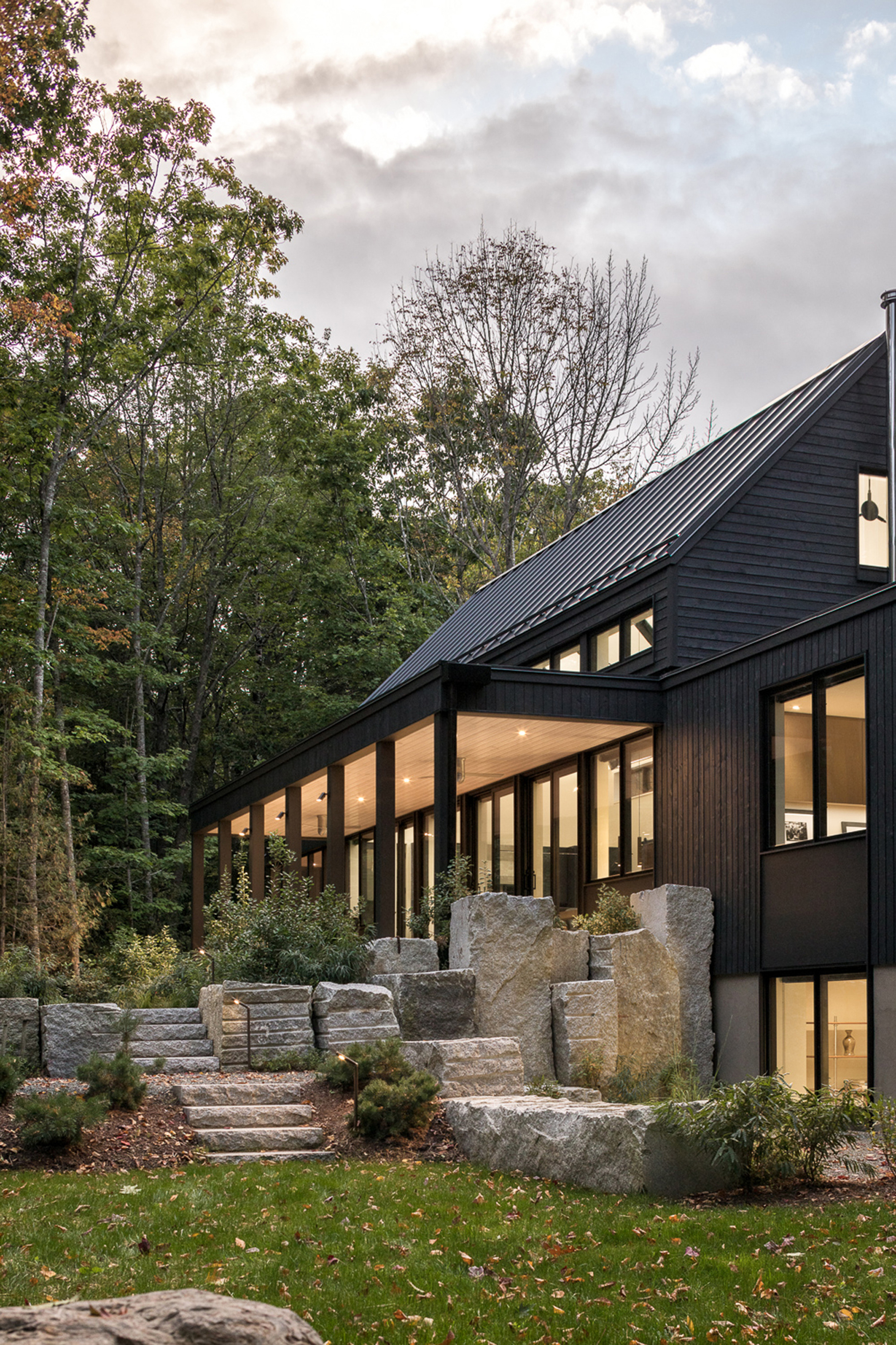 Black-stained wood facade with clerestory windows, terraced stone steps, and boulders under cloudy sky