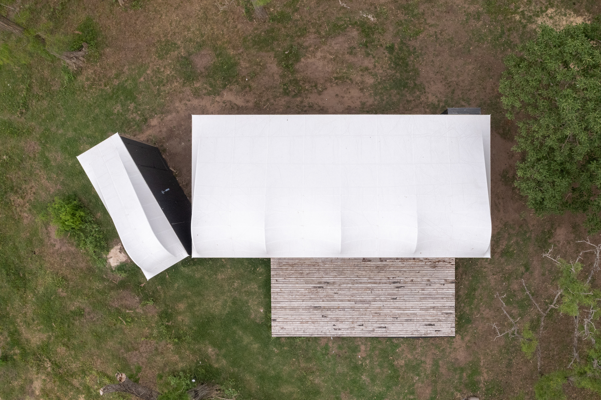 Aerial view of white barrel-vault roof and timber deck on patchy grass clearing