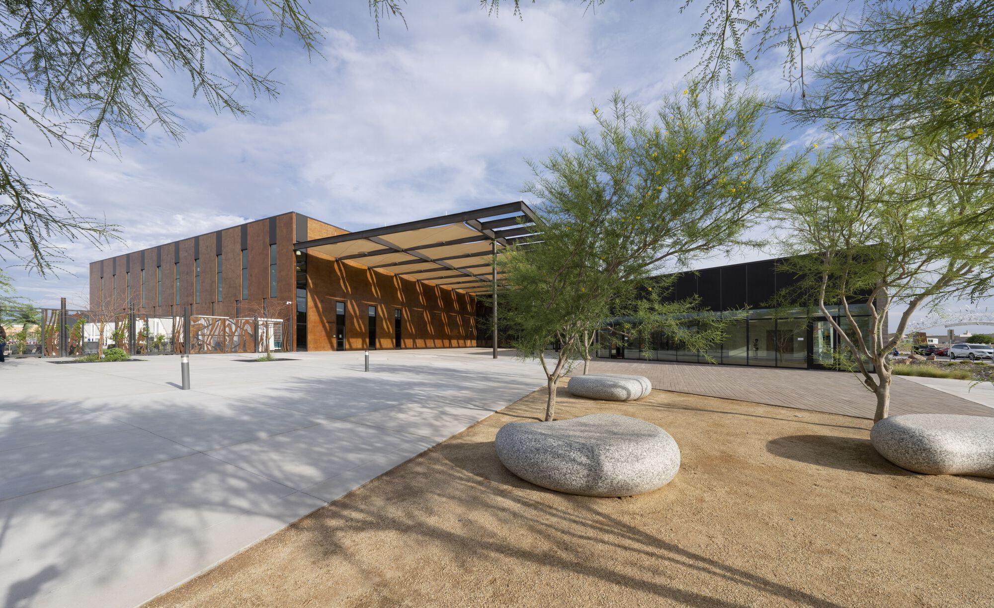 Covered entry plaza with corten steel screen and concrete paving under desert trees